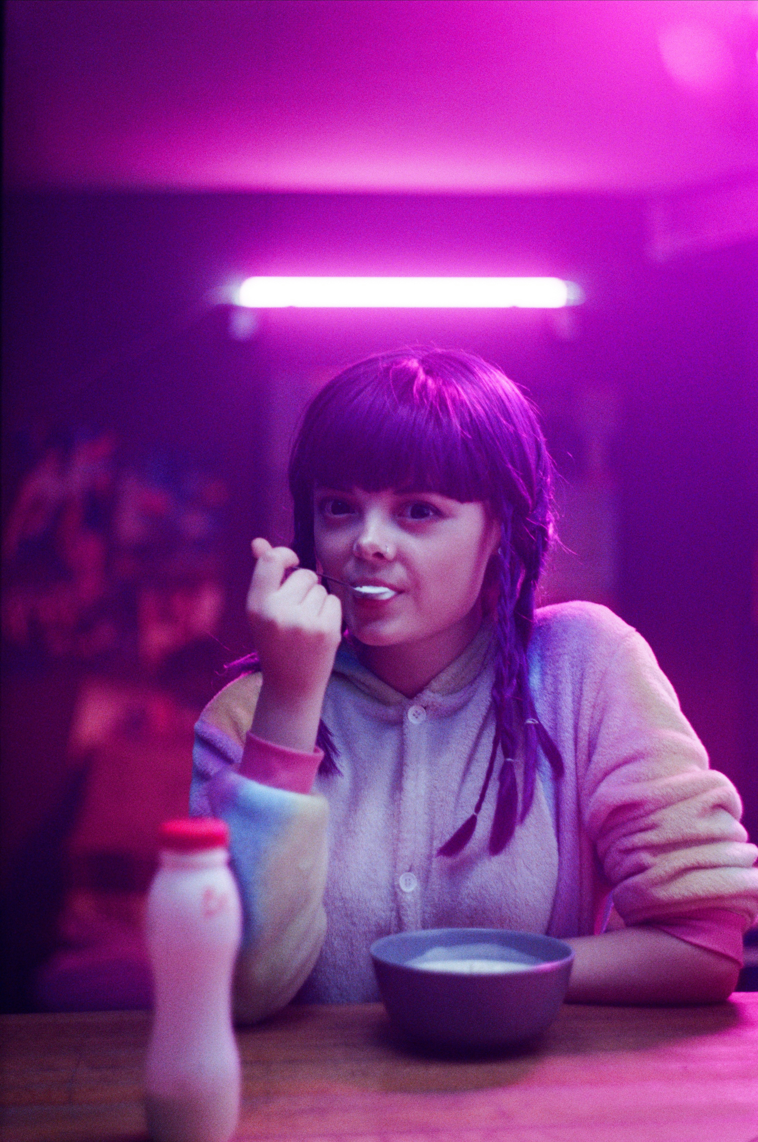 A young girl enjoying a bowl of cereal in a pink neon-lit room, capturing modern lifestyle visuals for social marketing campaigns.