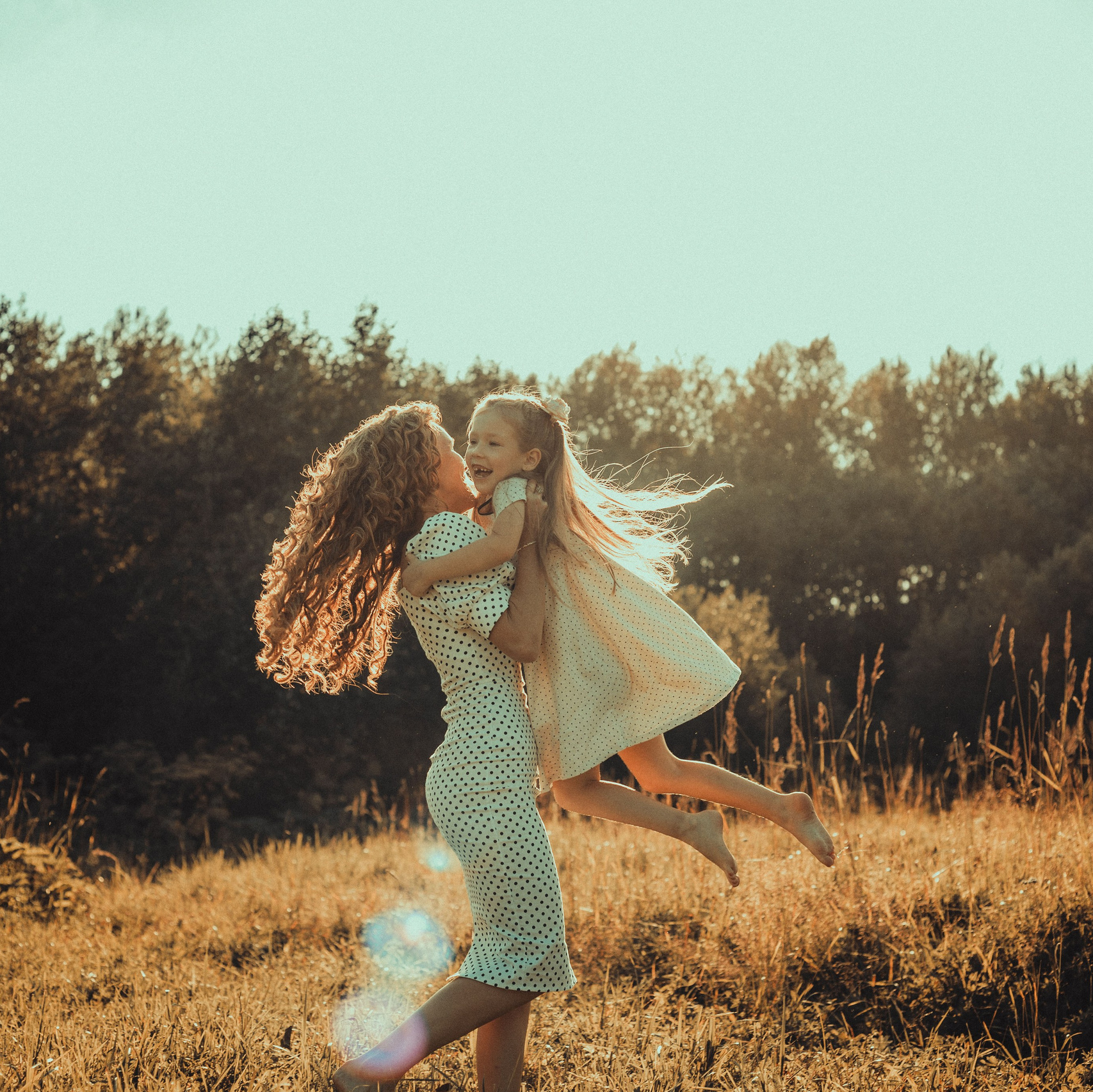 девушка в светлом свитере стоит на закате в лесу поймав лучик солнца с закрытыми глазами