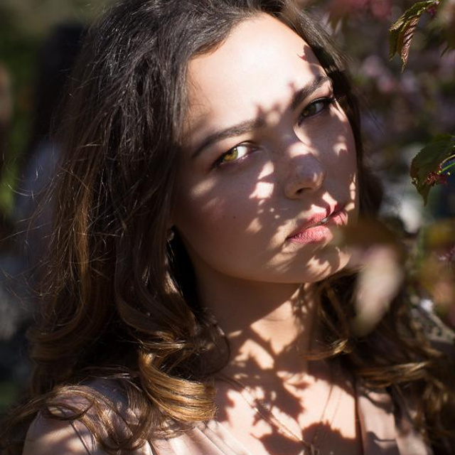 Портрет девушки в летний день, солнце проходит через листву и создает кружевной орнамент на ее лице