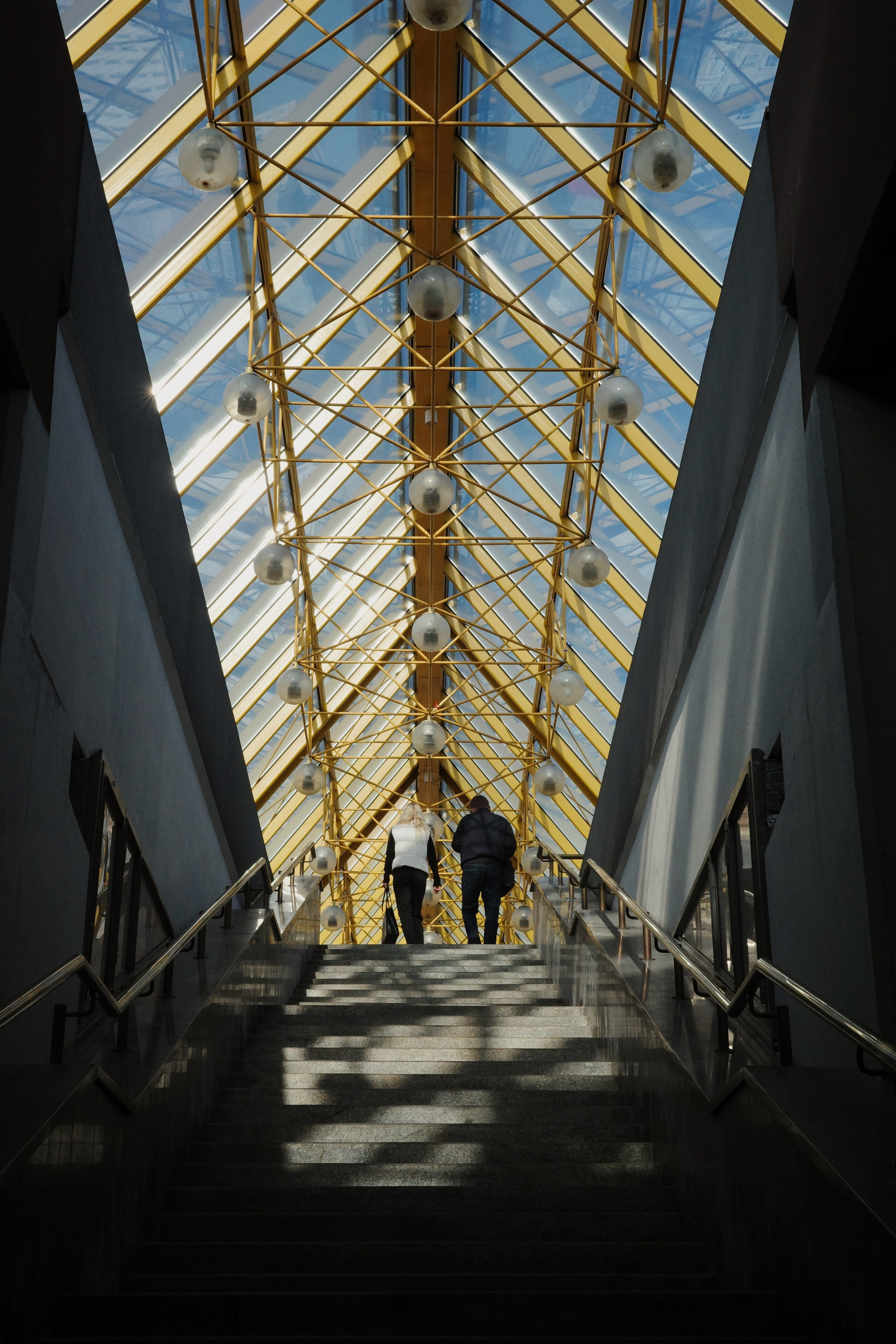 Внутри Андреевского пешеходного моста: жёлтый металлический каркас, стеклянная крыша