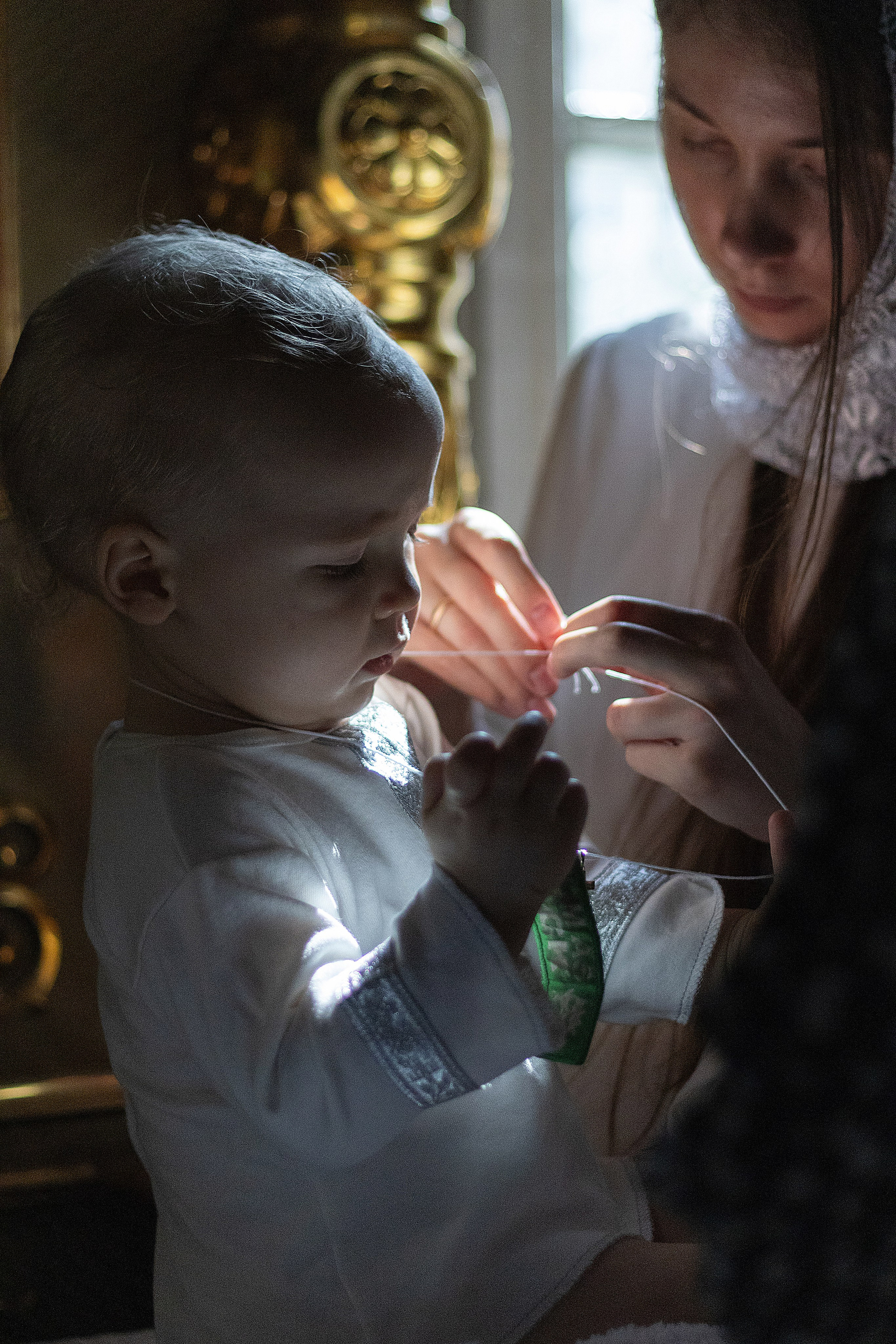 Младенец во время крещения на пеленальном столике сидит рядом с мамой на него одевают крестик