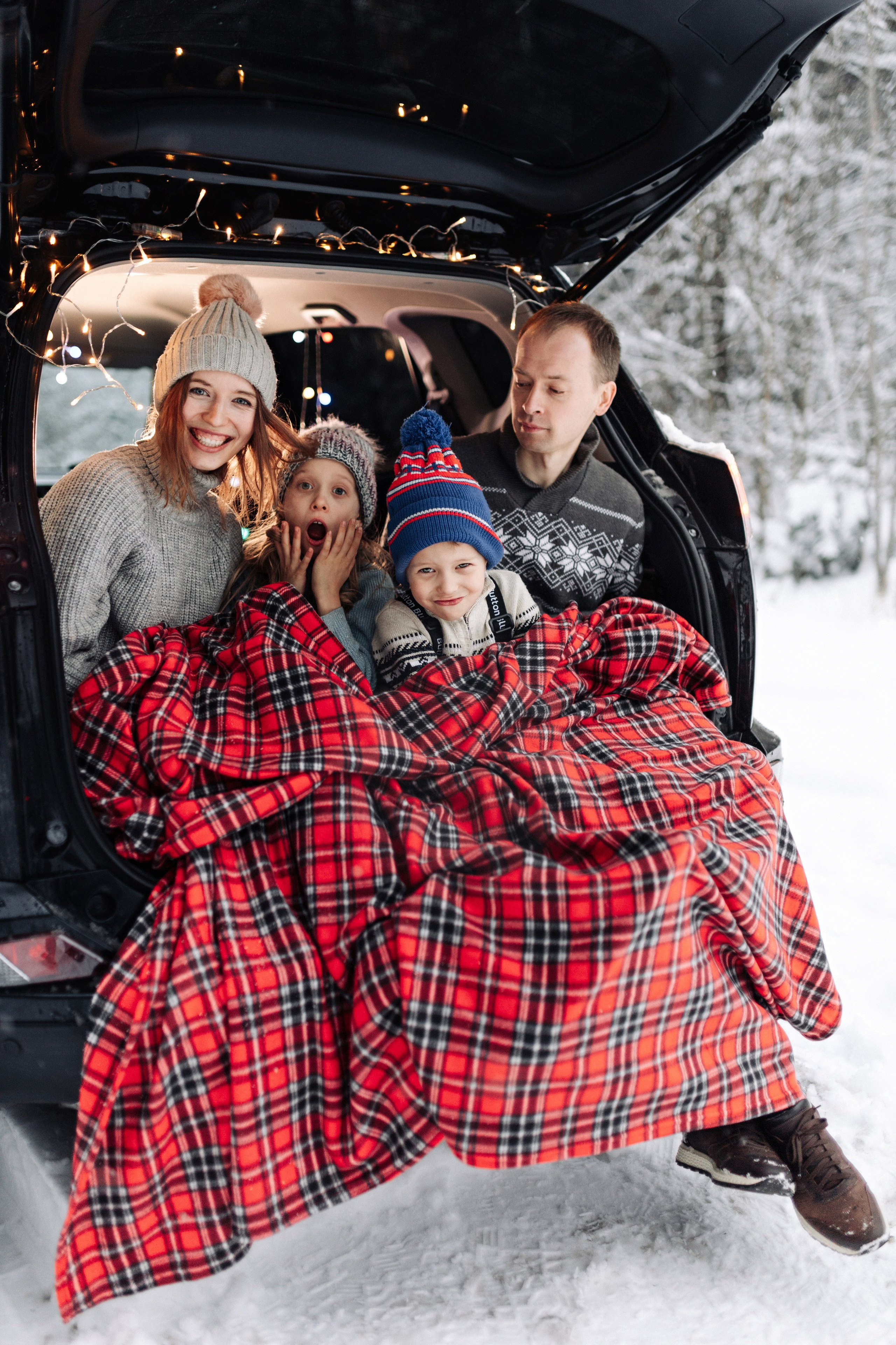 Новогодняя фотосессия семьи с детьми в Москве. Уютный зимний кадр с пледом и гирляндой в багажнике машины.