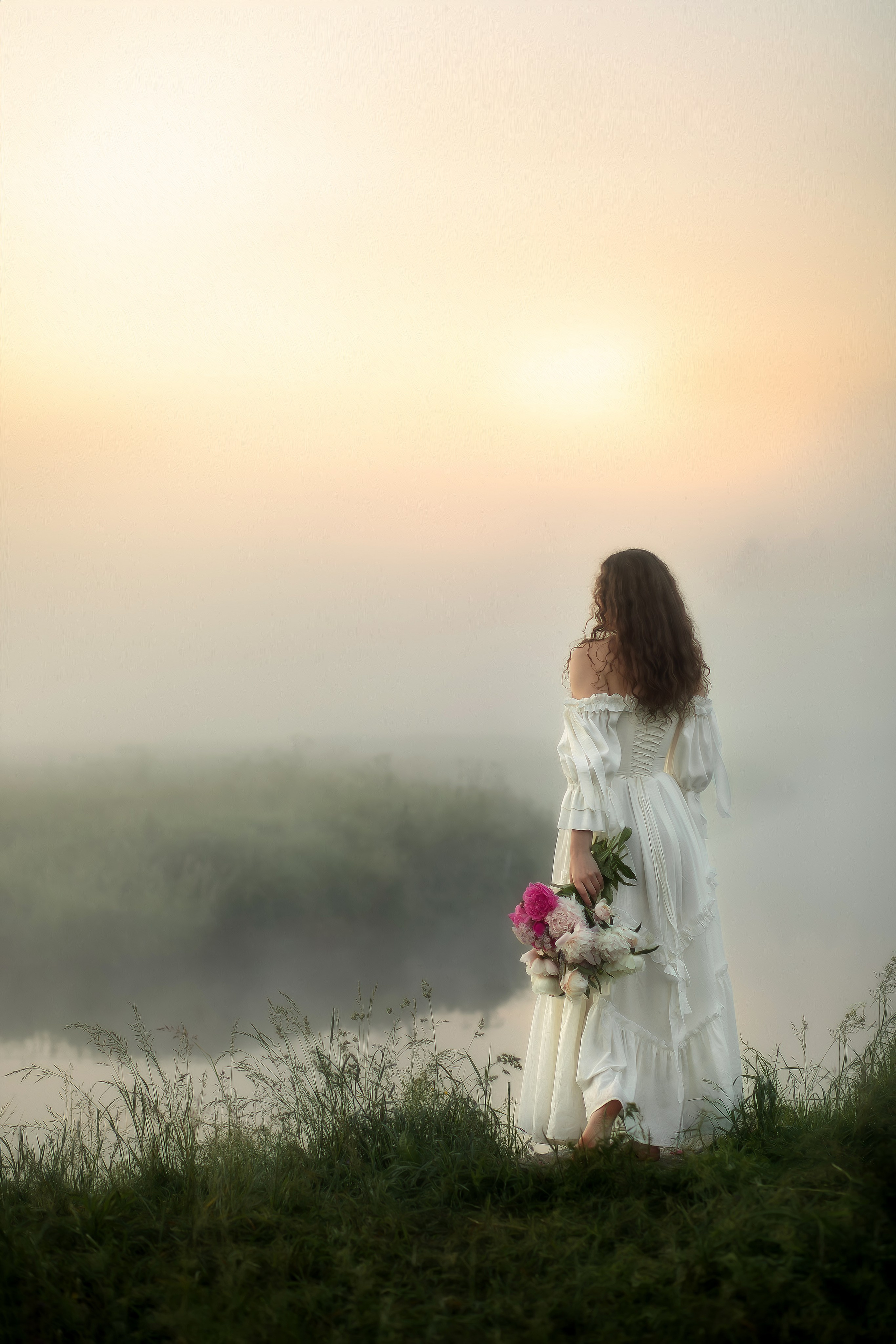 Девушка в белом платье стоит у воды на фоне тумана и рассветного света, в руках букет пионов.