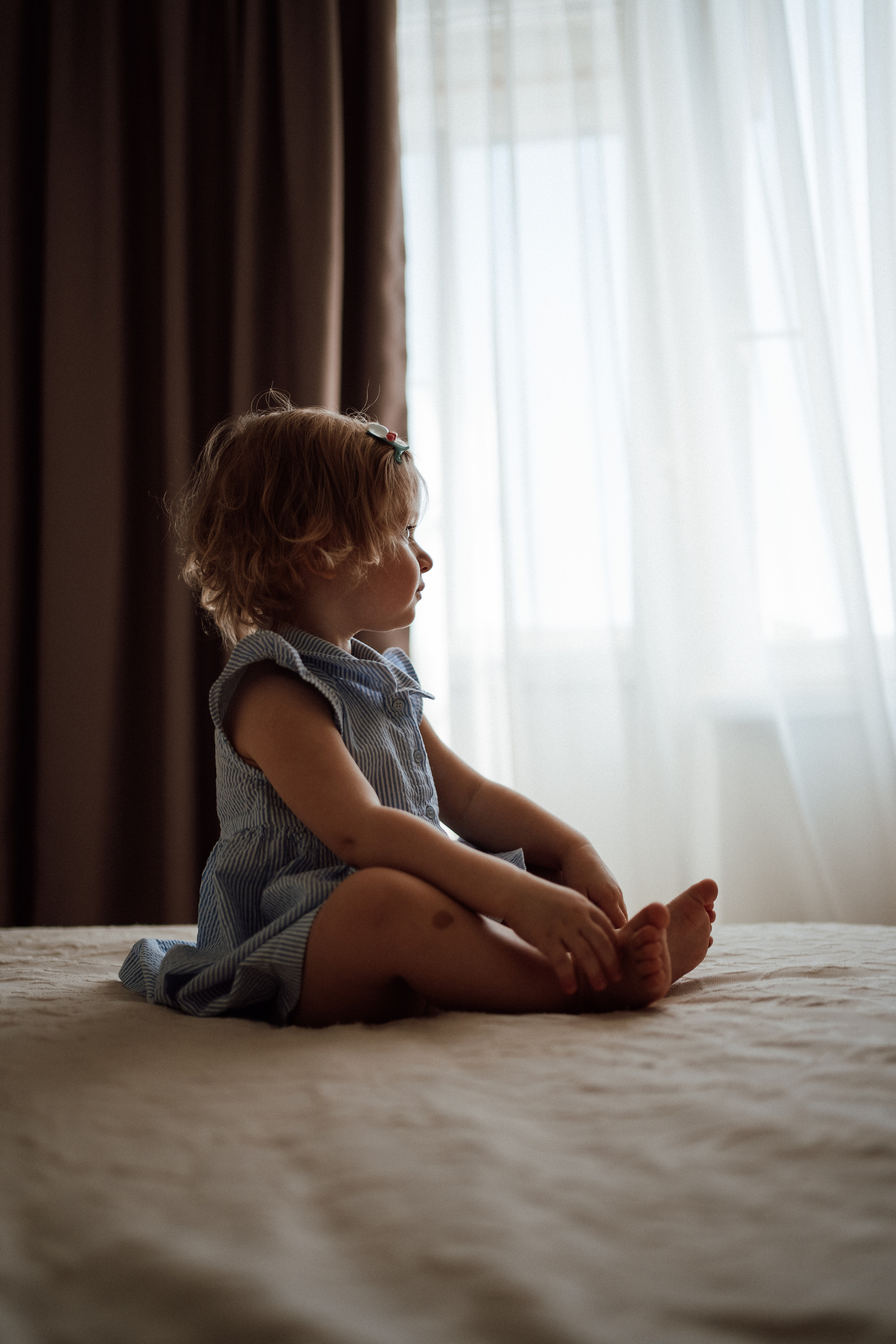 Маленькая девочка в контровом свете сидит напротив окна