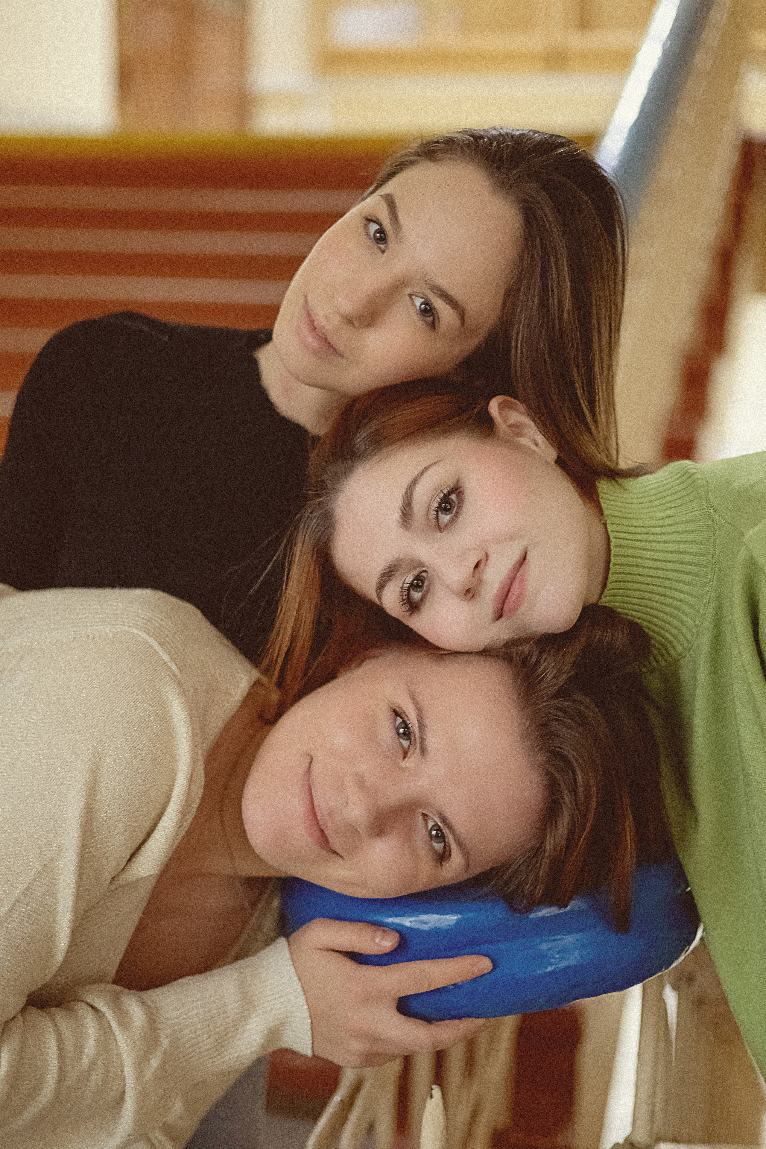 Три женщины позируют рядом на лестнице, положив головы друг на друга. Они нежно улыбаются, излучая теплоту и дружелюбие.