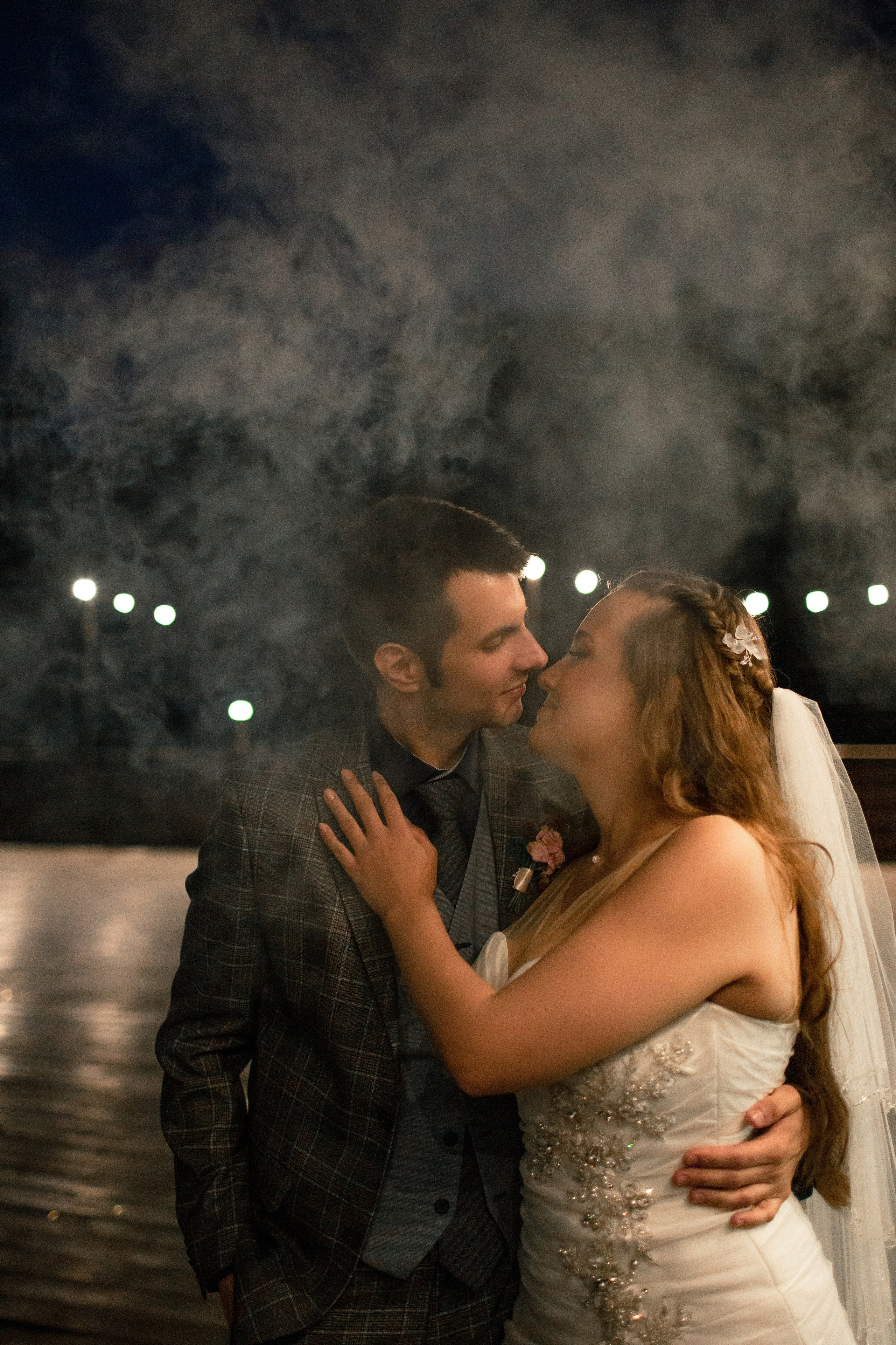 Художественная свадебная фотография: жених и невеста целуются в дымке на фоне ночных огней.