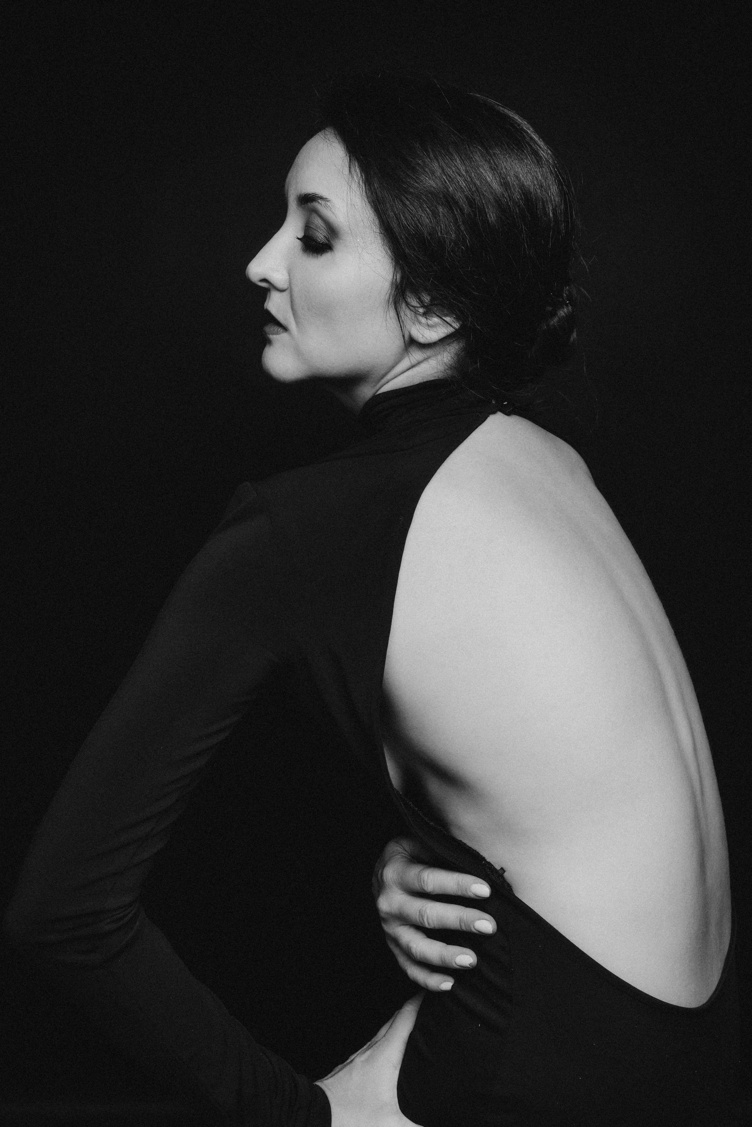 Художественный портрет женщины в черном платье с открытой спиной на темном фоне, черно-белое фото.