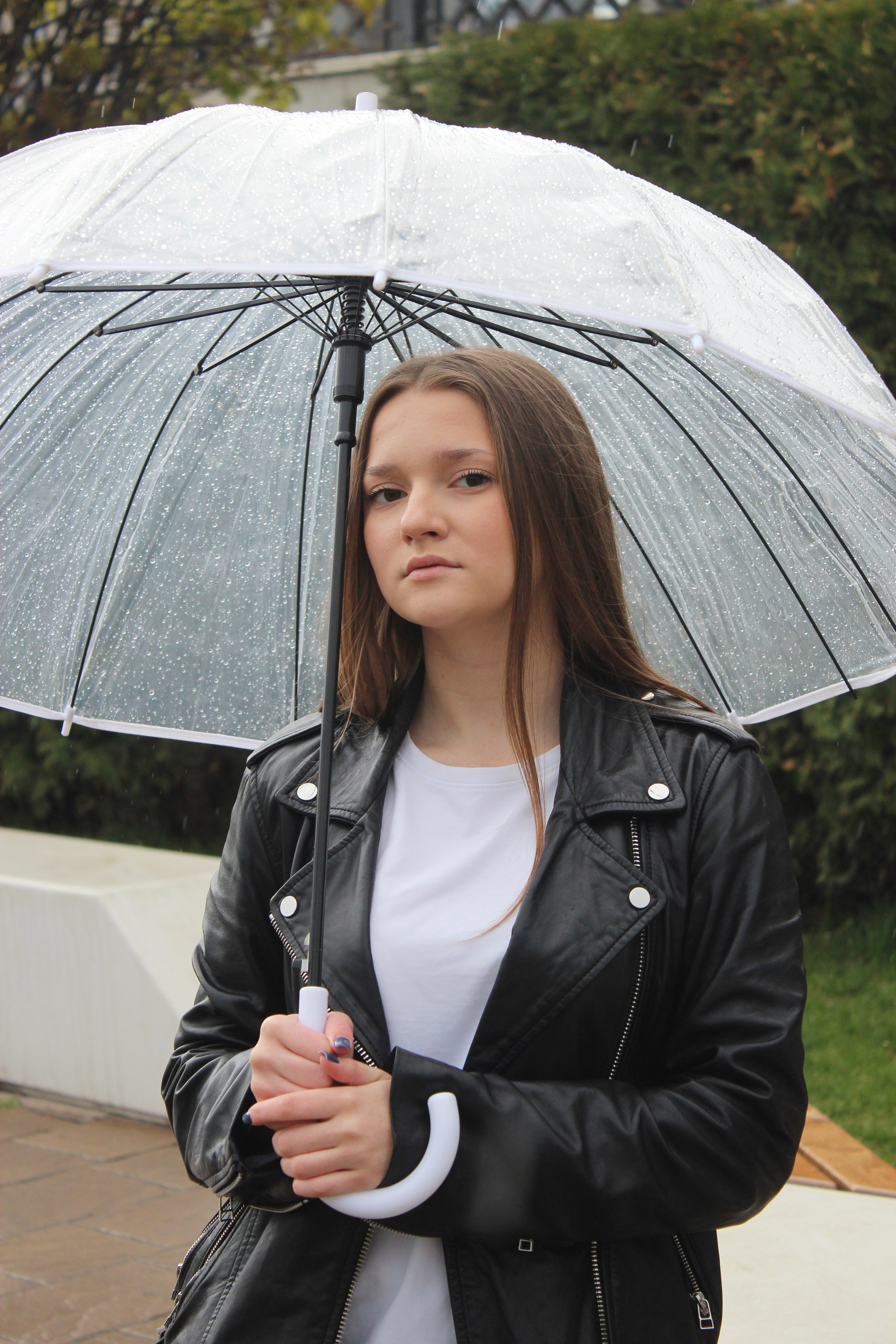 "Street photo shooting for young woman in a black leather jacket holds a clear umbrella in the rain".