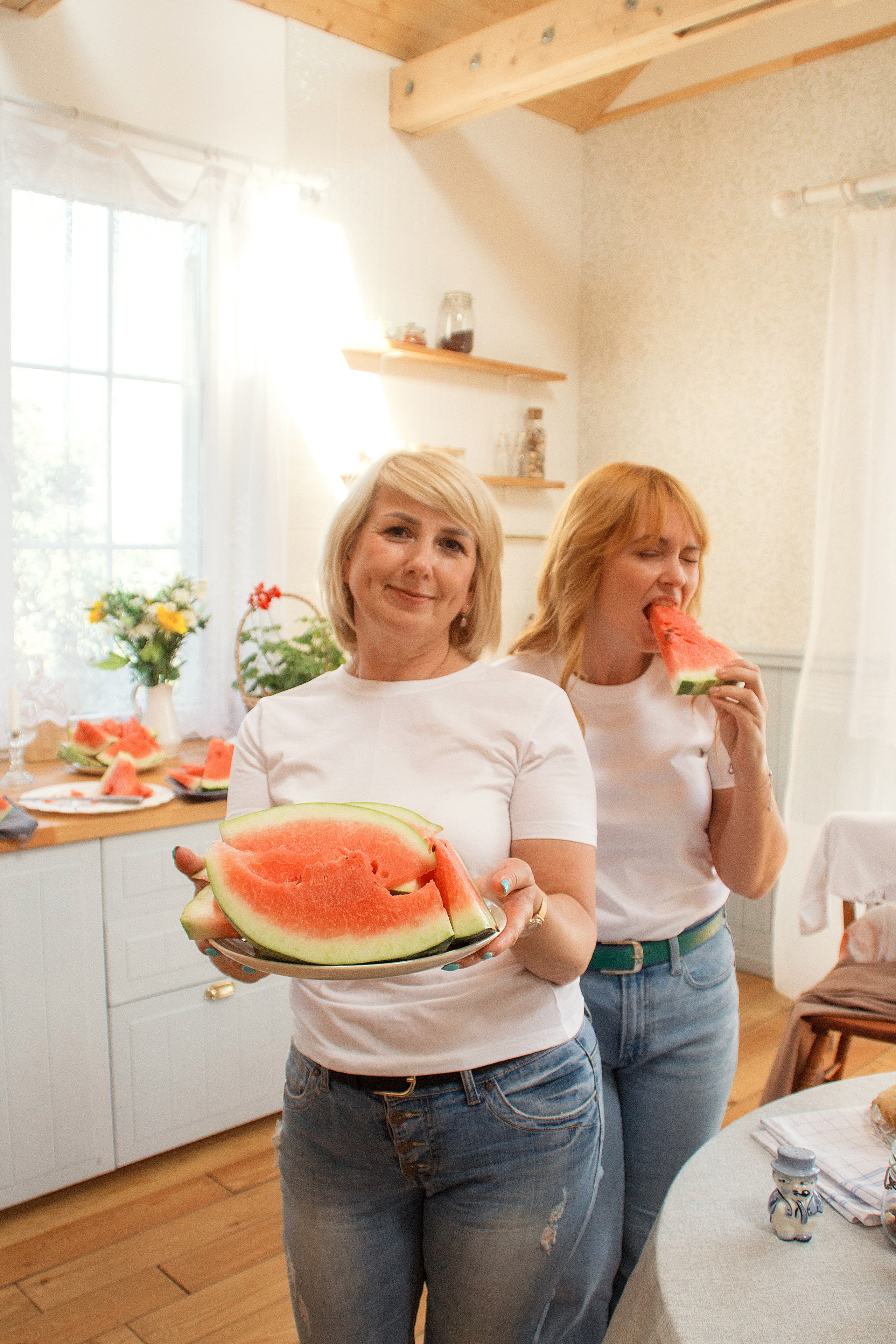 Подруги в белых футболках и джинсах едят красный сочный арбуз и весело проводят беседу.