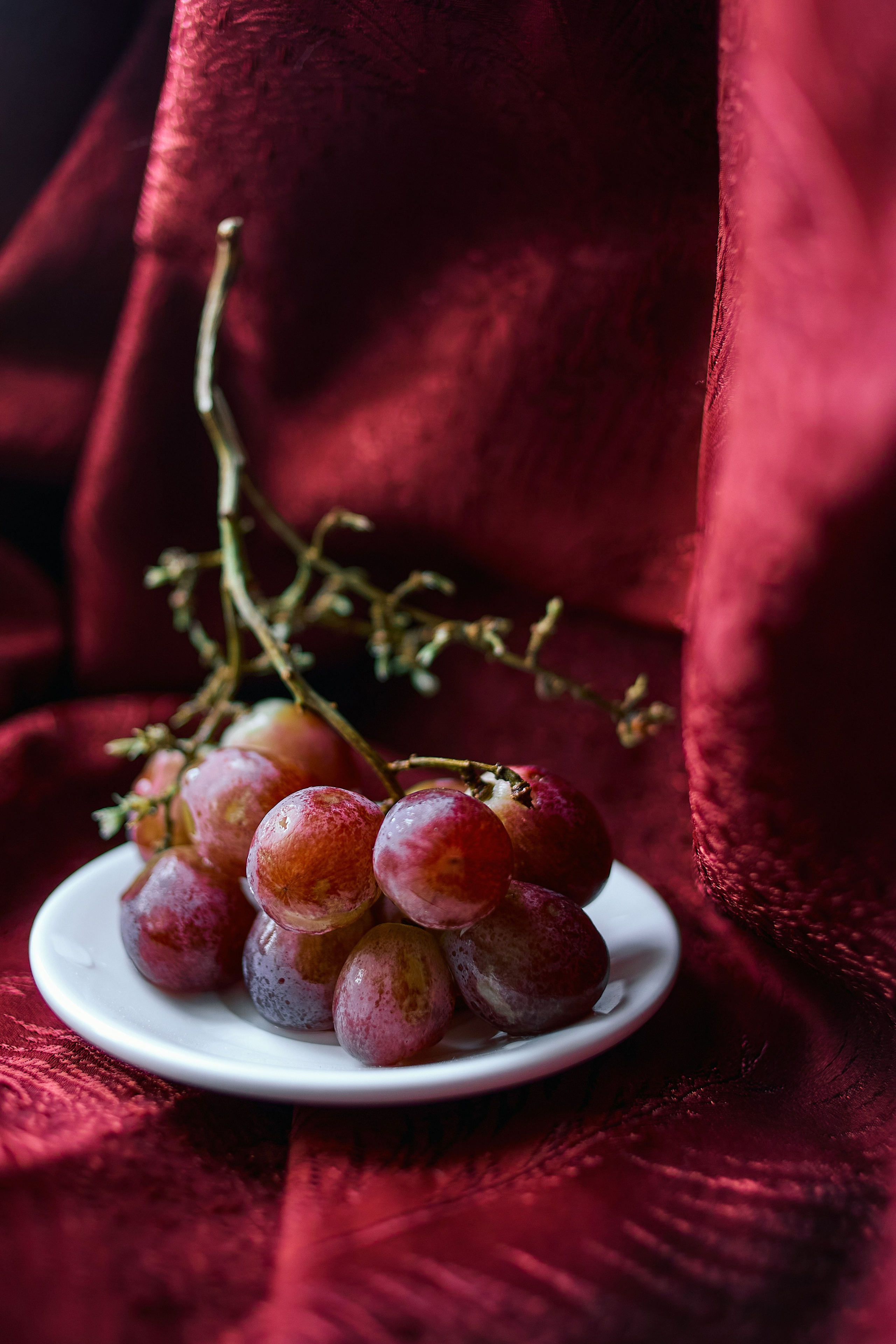 Виноград в тарелке на фоне красивой алой ткани