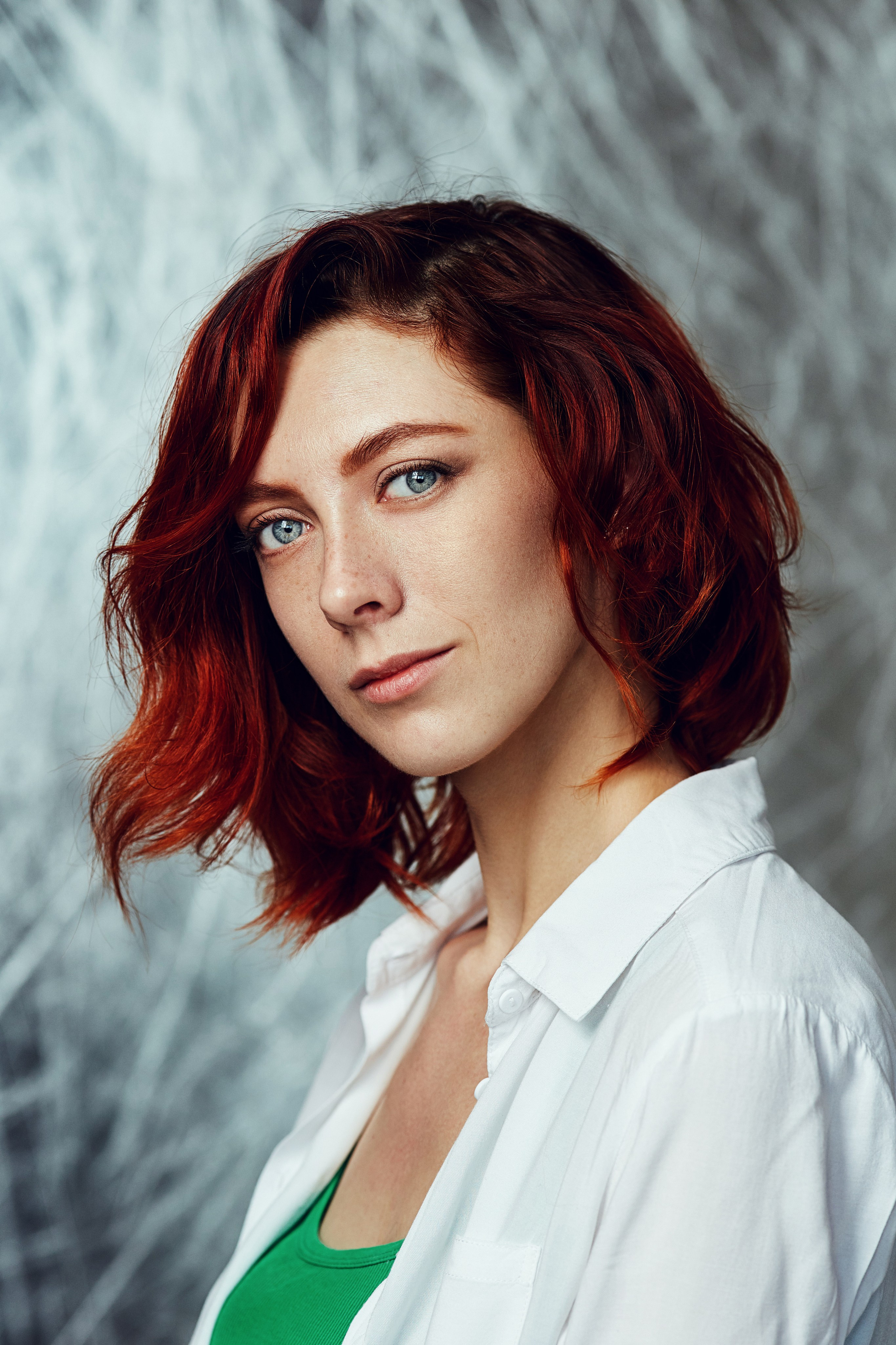 Женский портрет в студии. Модель с рыжими волосами и голубыми глазами позирует в белой рубашке на серебристом фоне