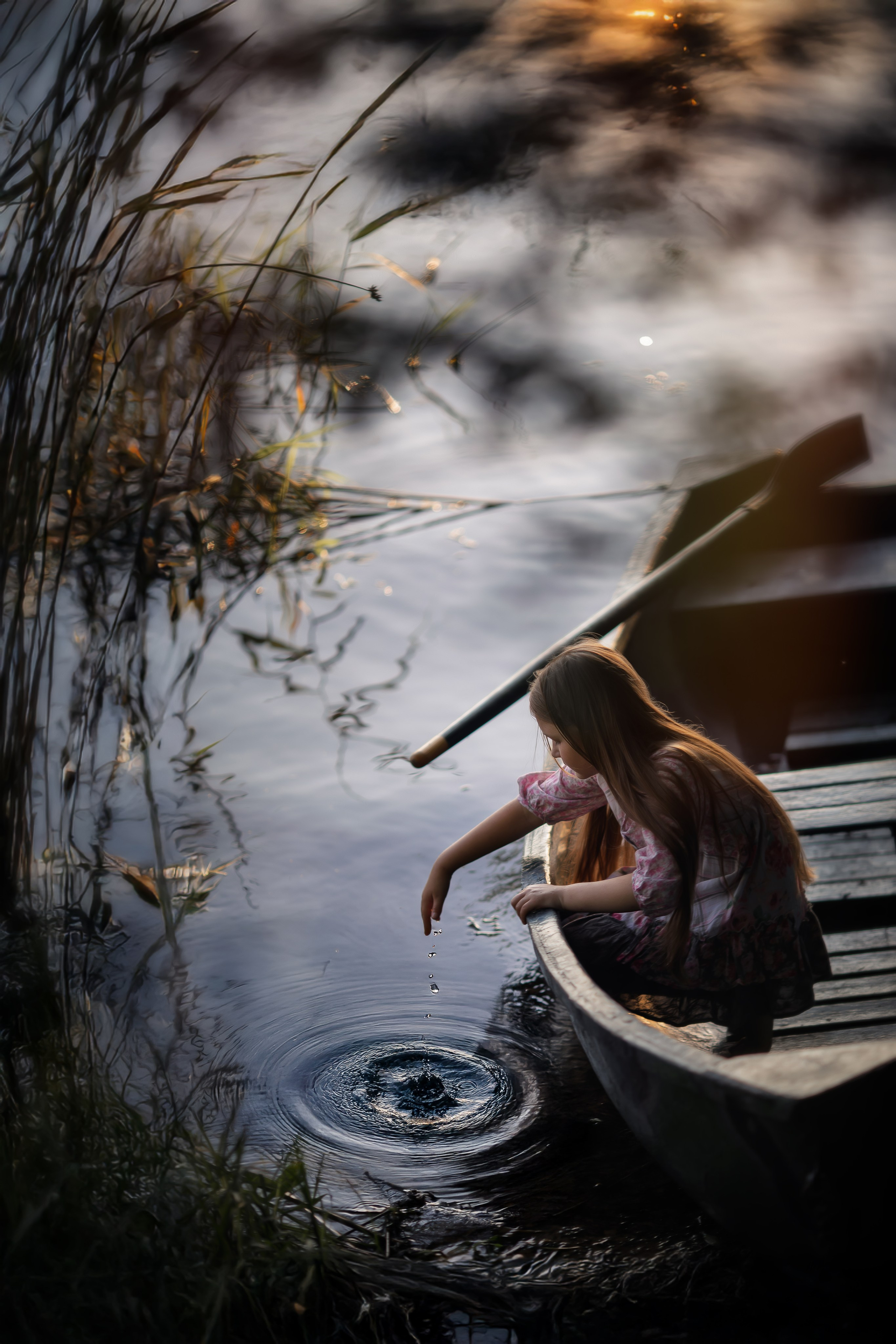 Девочка на деревянной лодке, на закате среди прибрежной травы.