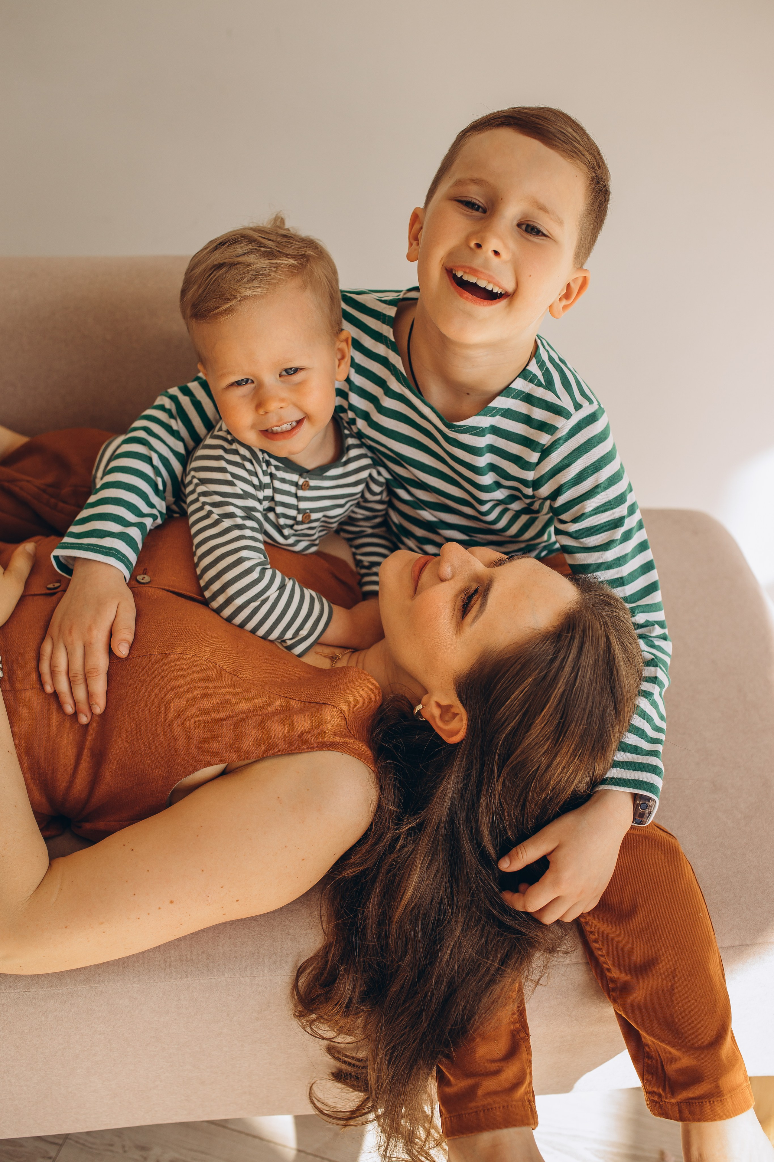 Счастливая мама в оранжевом комбинезоне на фотосессии с сыновьями в светлом интерьере. Детский и семейный фотограф Маруся Самылкина в Санкт-Петербурге.