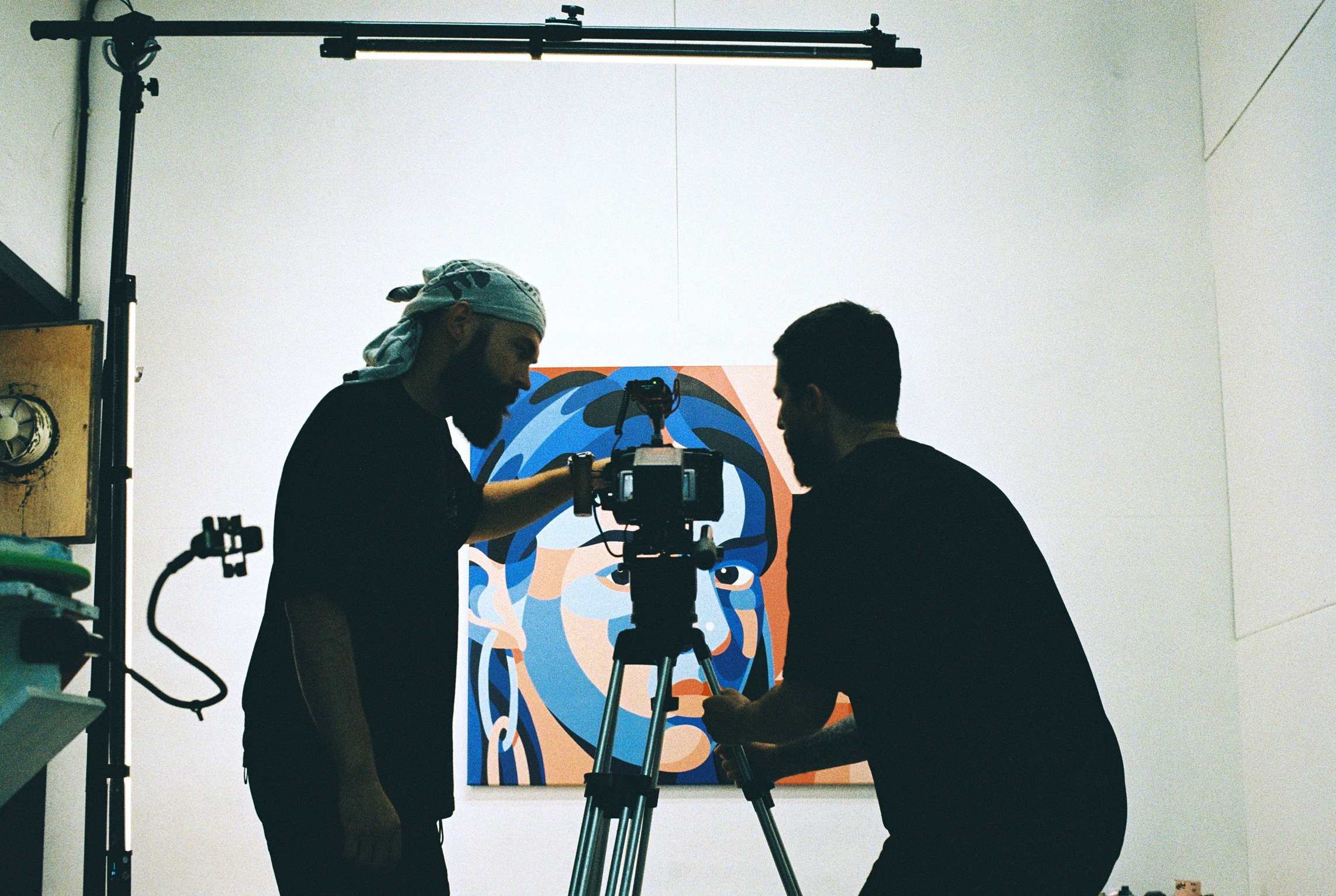 Оператор и режиссёр двигают штатив с кинокамерой к картине на стене