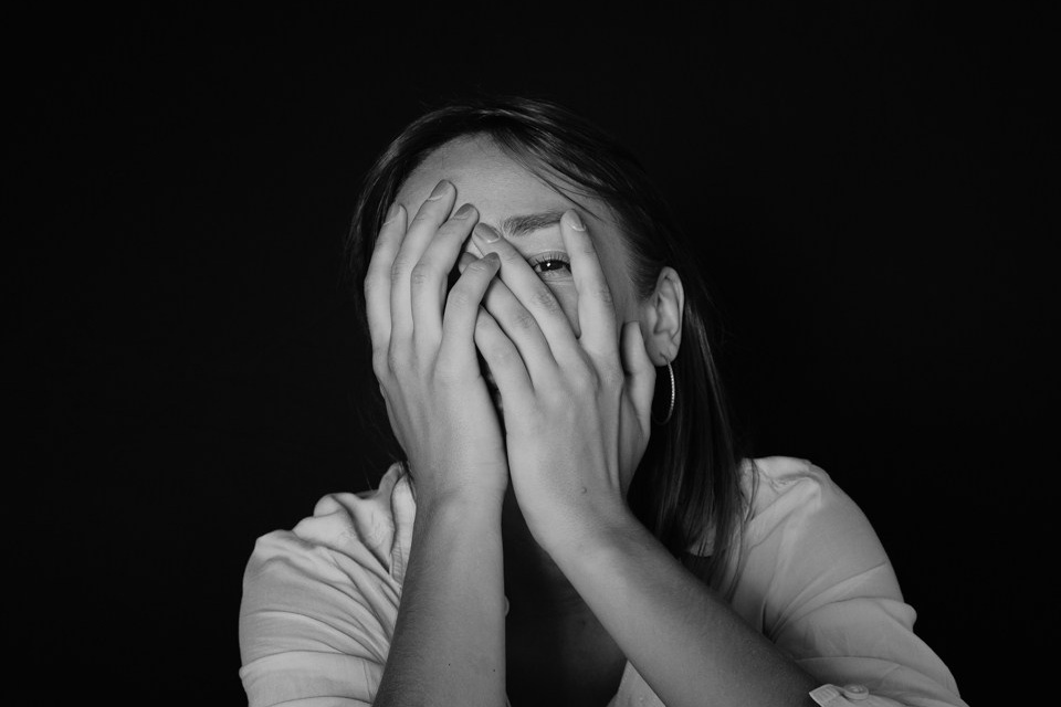 Фотоснимок девушки закрывавший лицо руками на черной фоне