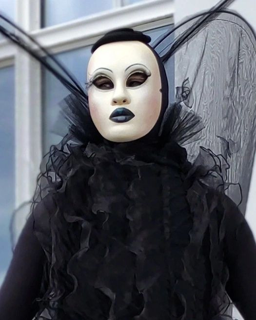 Мим в белой маске с чёрными губами и чёрными крыльями ждёт гостей у окна.