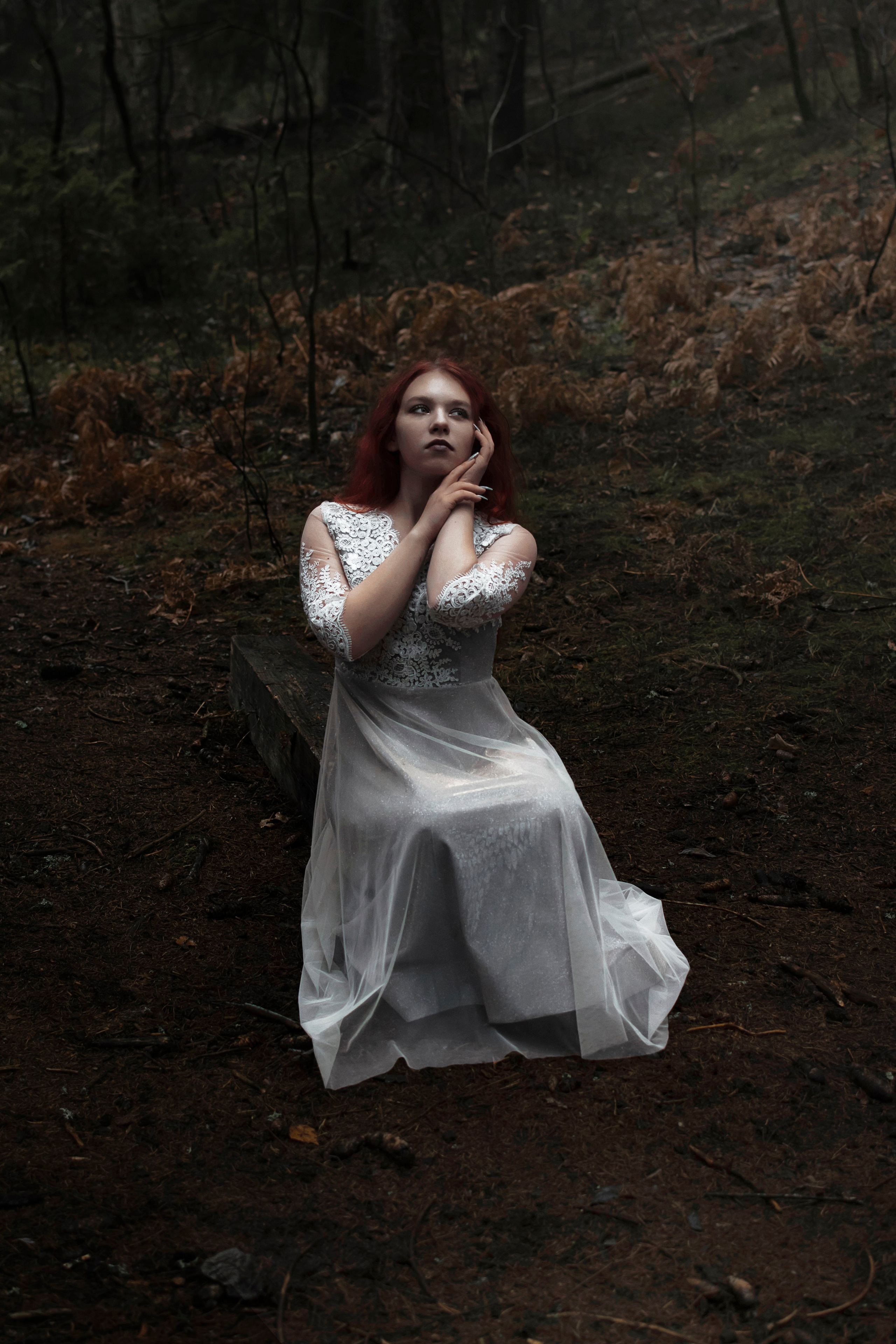 Молодая девушка сидит в лесу в белом платье.