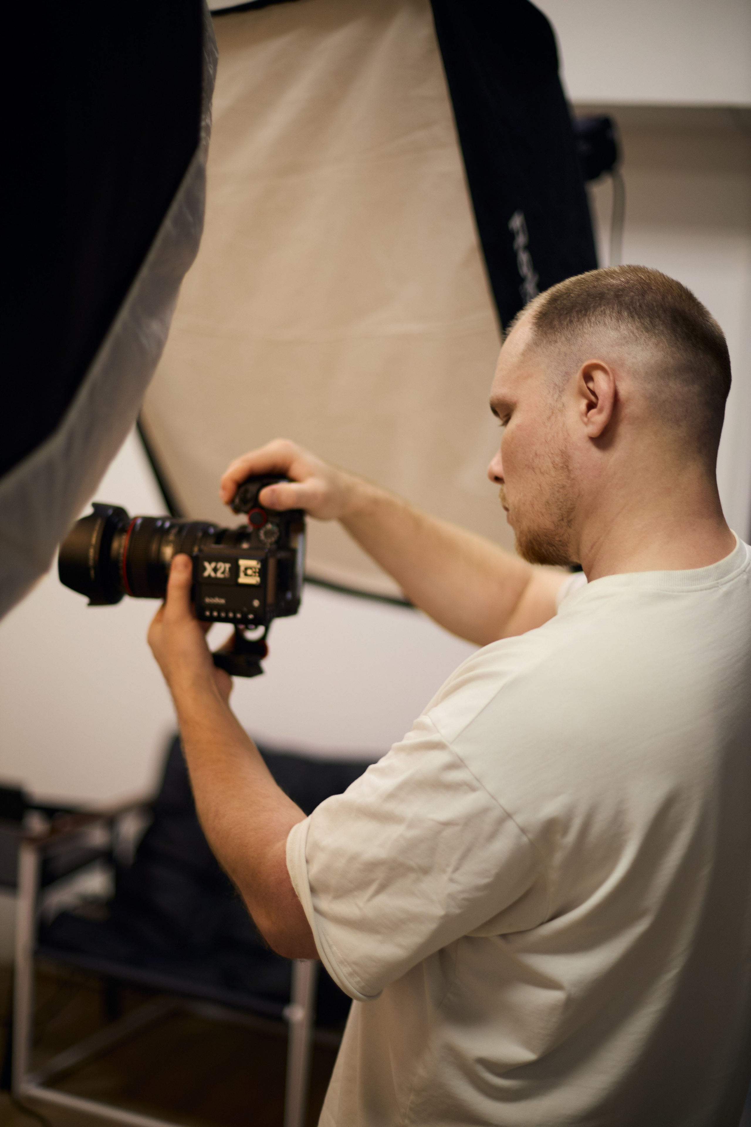 Фотограф с камерой на фоне студийного освещения во время работы — процесс профессиональной выездной съемки.