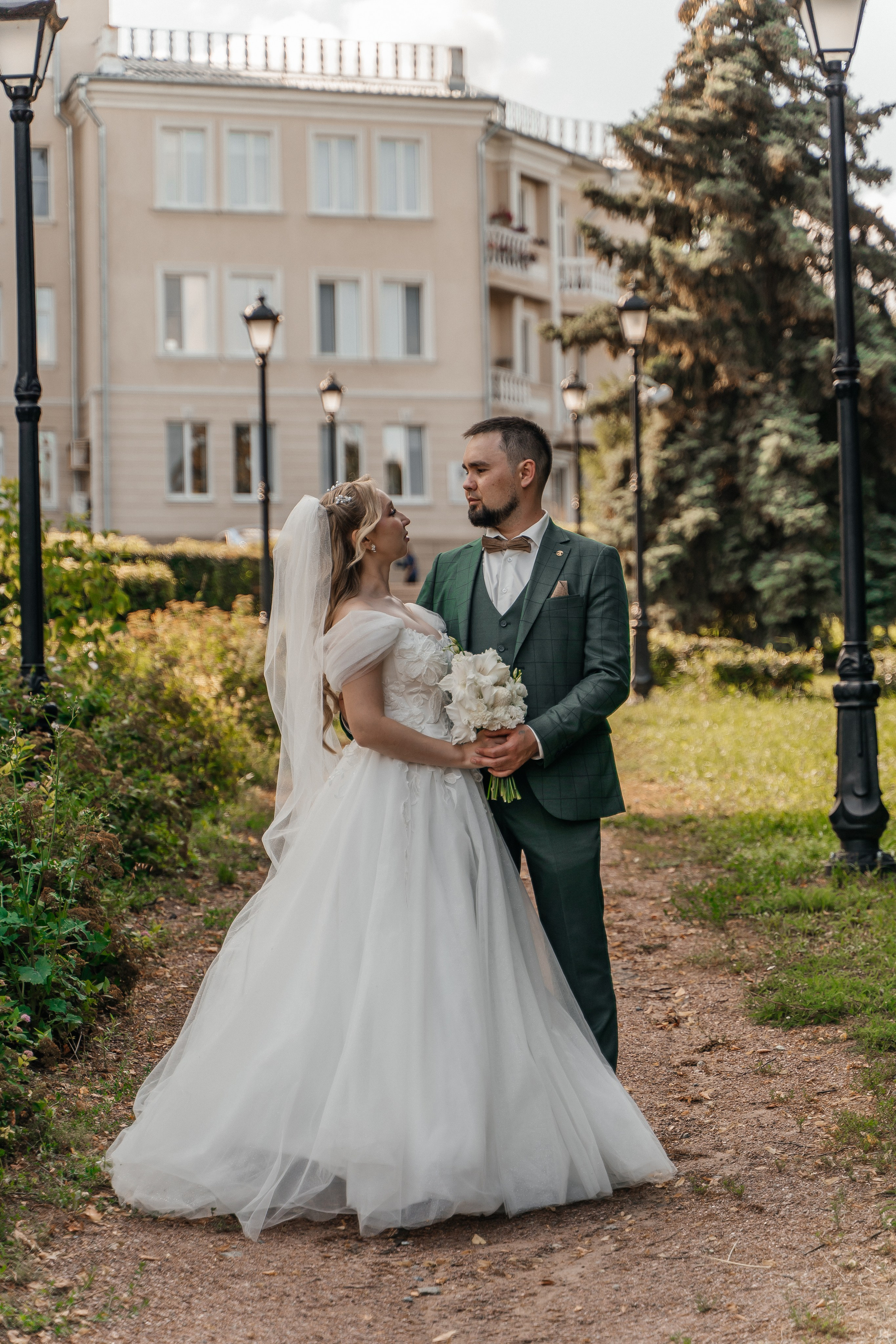 Портрет невесты с фатой в лучах заходящего солнца в сосновом лесу.Жених в стильном костюме прислонился к кирпичной стене, смотрит задумчиво в камеру.Молодожены идут, держась за руки, по пустынной городской улице в вечерних огнях.