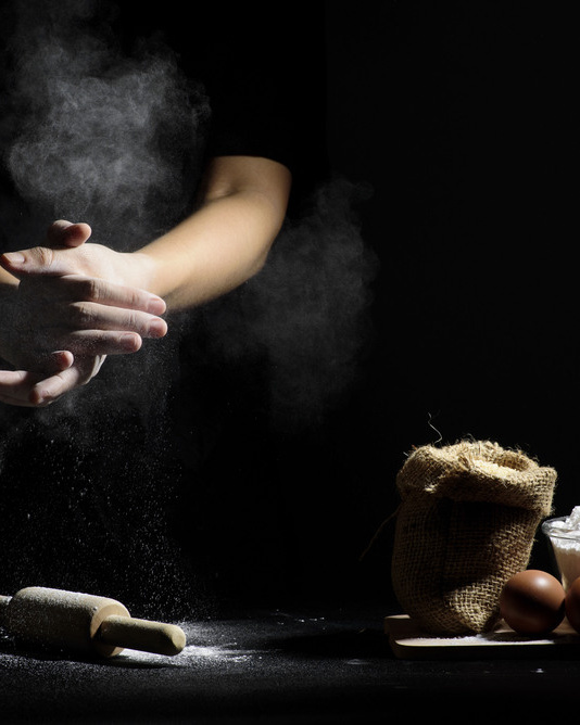 мужчина хлебопек потирает руки в муке, рядом стоит ковш с мукой