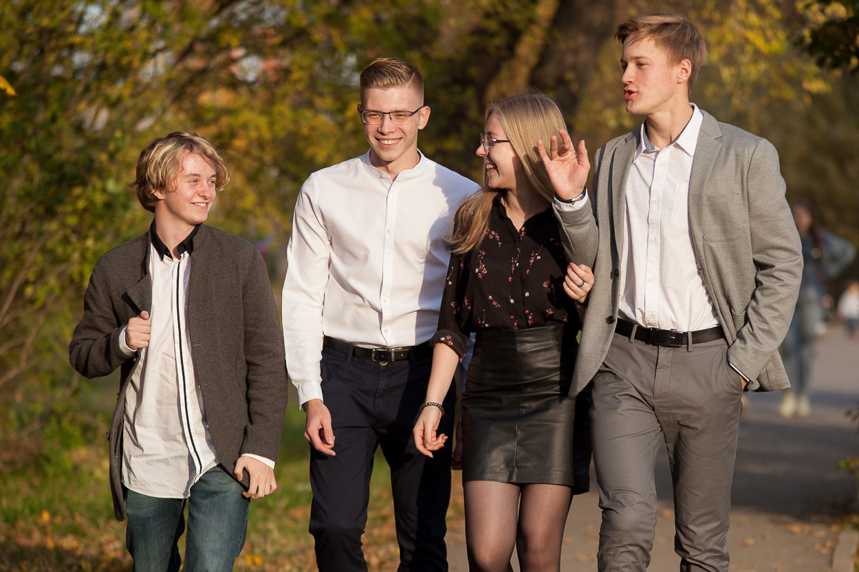 четыре выпускника идут по дорожке в осеннем парке и разговаривают между собой.