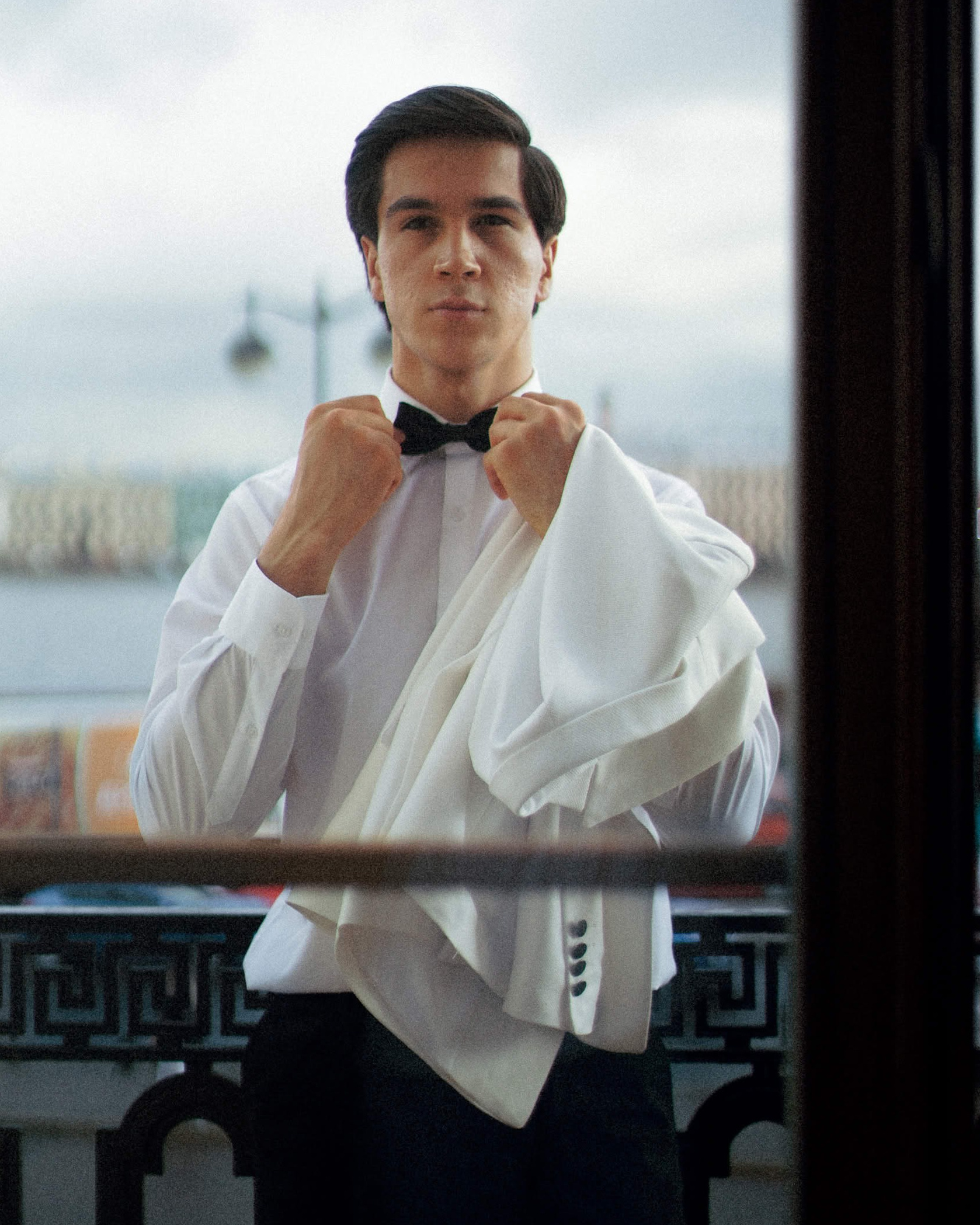 Утро жениха — подготовка к свадьбе, завязывание бабочки у окна, стильный кадр в формате editorial