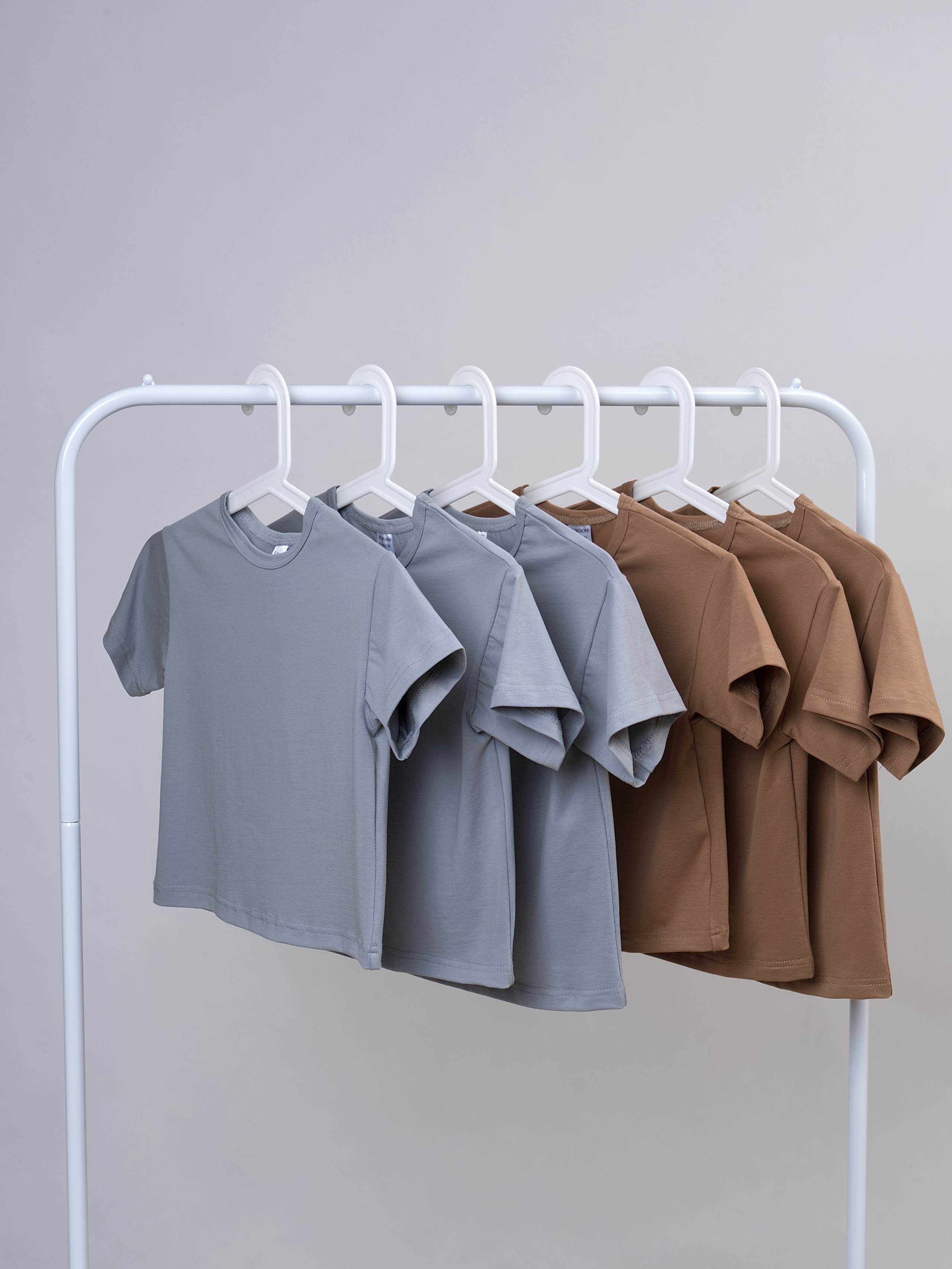Фото детских футболок в серых и коричневых цветах на вешалке снято в фото студии.