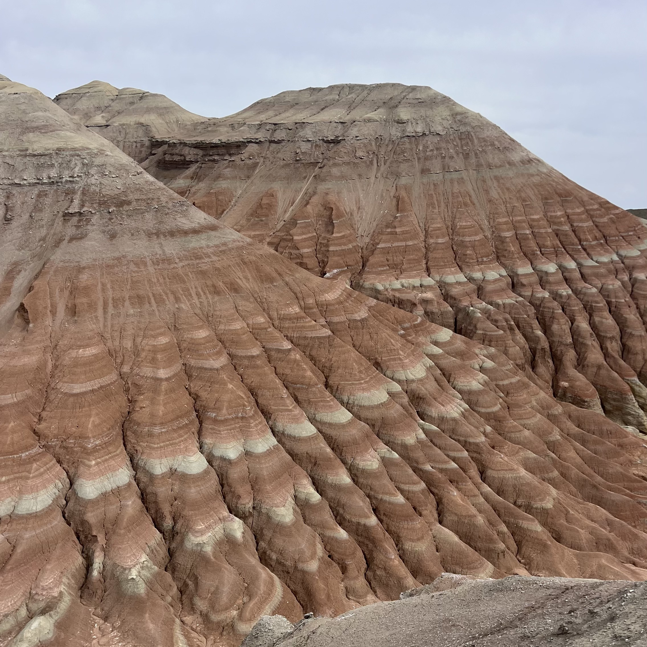 Человек стоит у подножия замерзшего водопада Медвежий среди заснеженных скал. Вода продолжает течь, частично покрытая льдом, создавая красивый контраст между движущейся водой и ледяными наростами. Земля вокруг покрыта снегом, создавая зимнюю атмосферу. Человек одет в теплую одежду — синее пальто с капюшоном и розовую шапку.