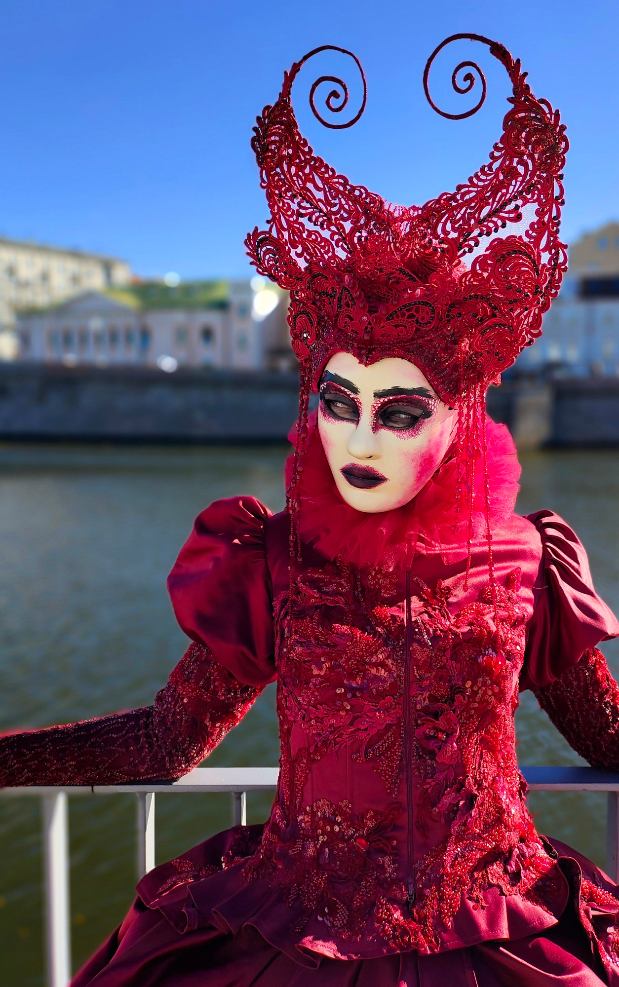 Мим в бордовом головном уборе и с маской на лице позирует фотографу.