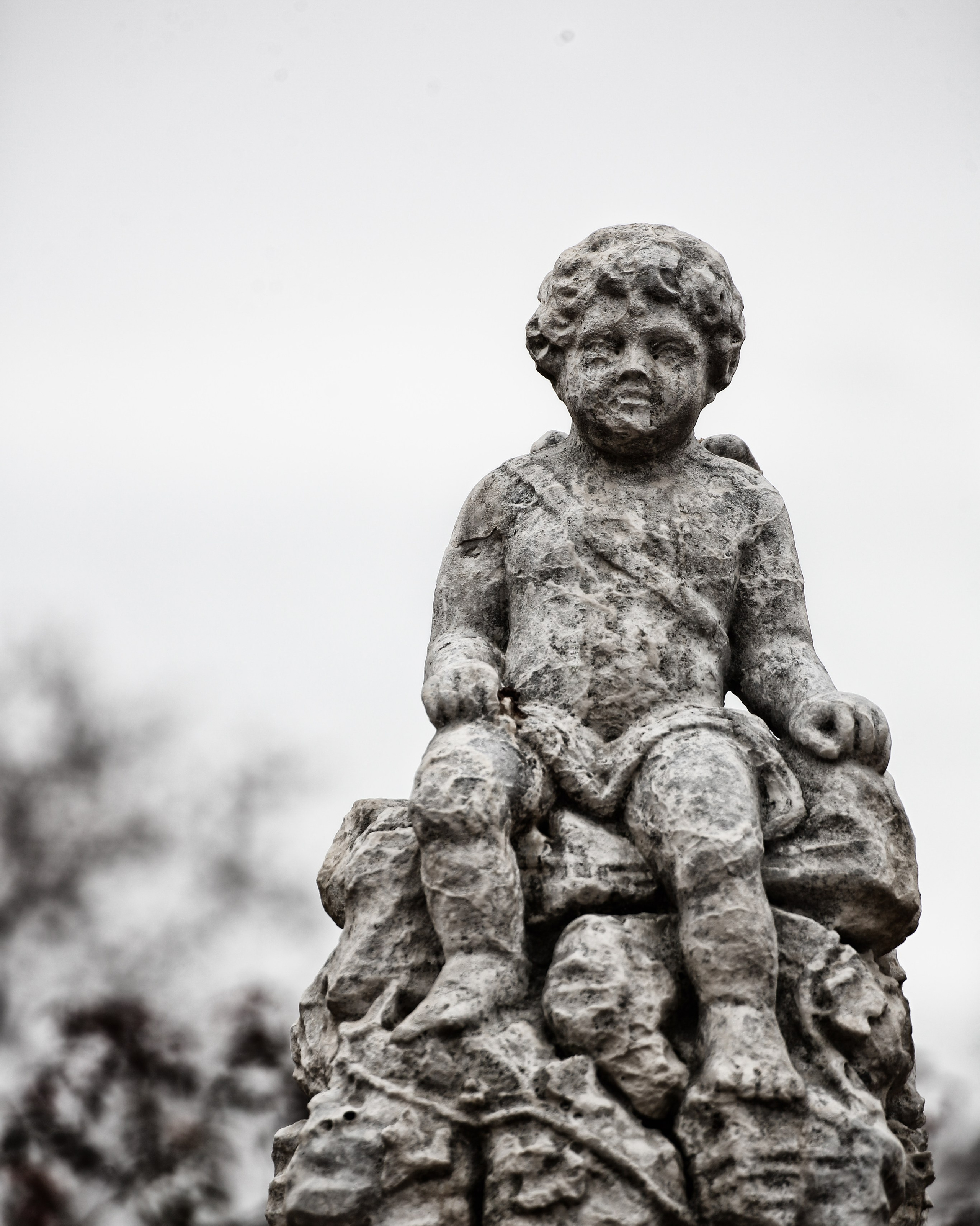Каменная скульптура сидящего херувима с кудрявыми волосами, старинное надгробие, черно-белое фото кладбищенской скульптуры