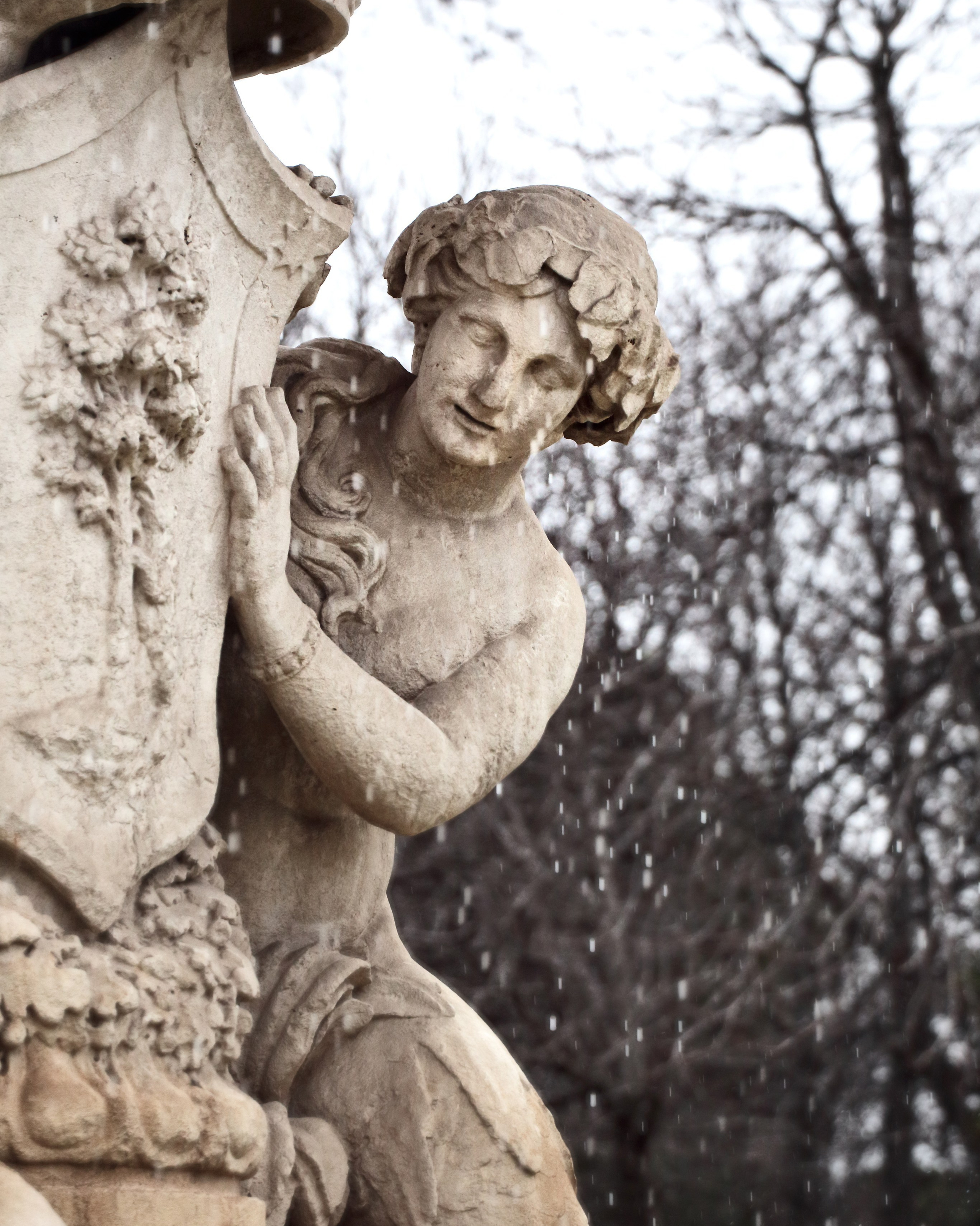 Каменная скульптура фигуры обнимающей колонну во время снегопада, падающий снег, классическая садовая скульптура