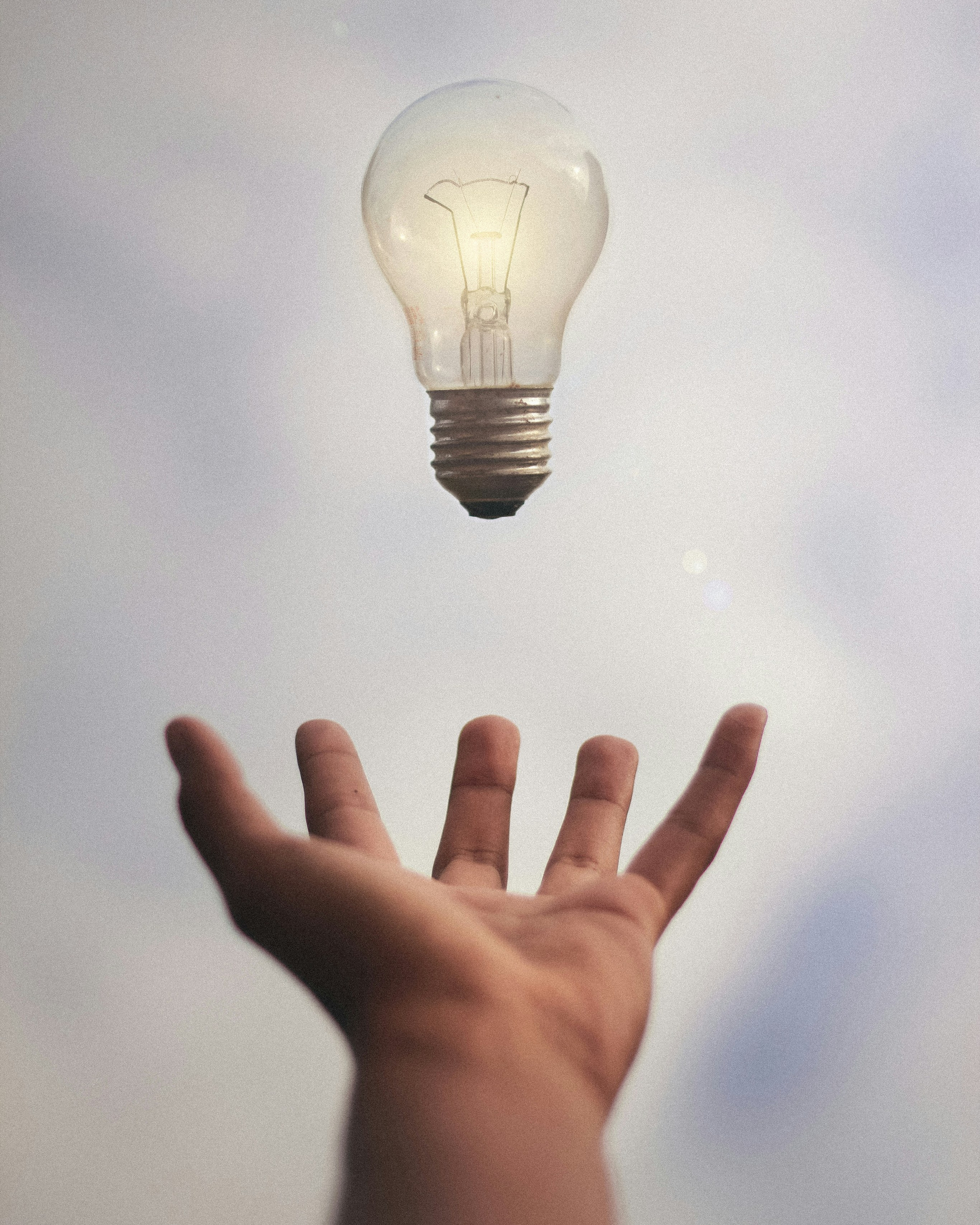 A hand reaching up towards a floating light bulb, symbolizing creativity and innovation in the history of photography
