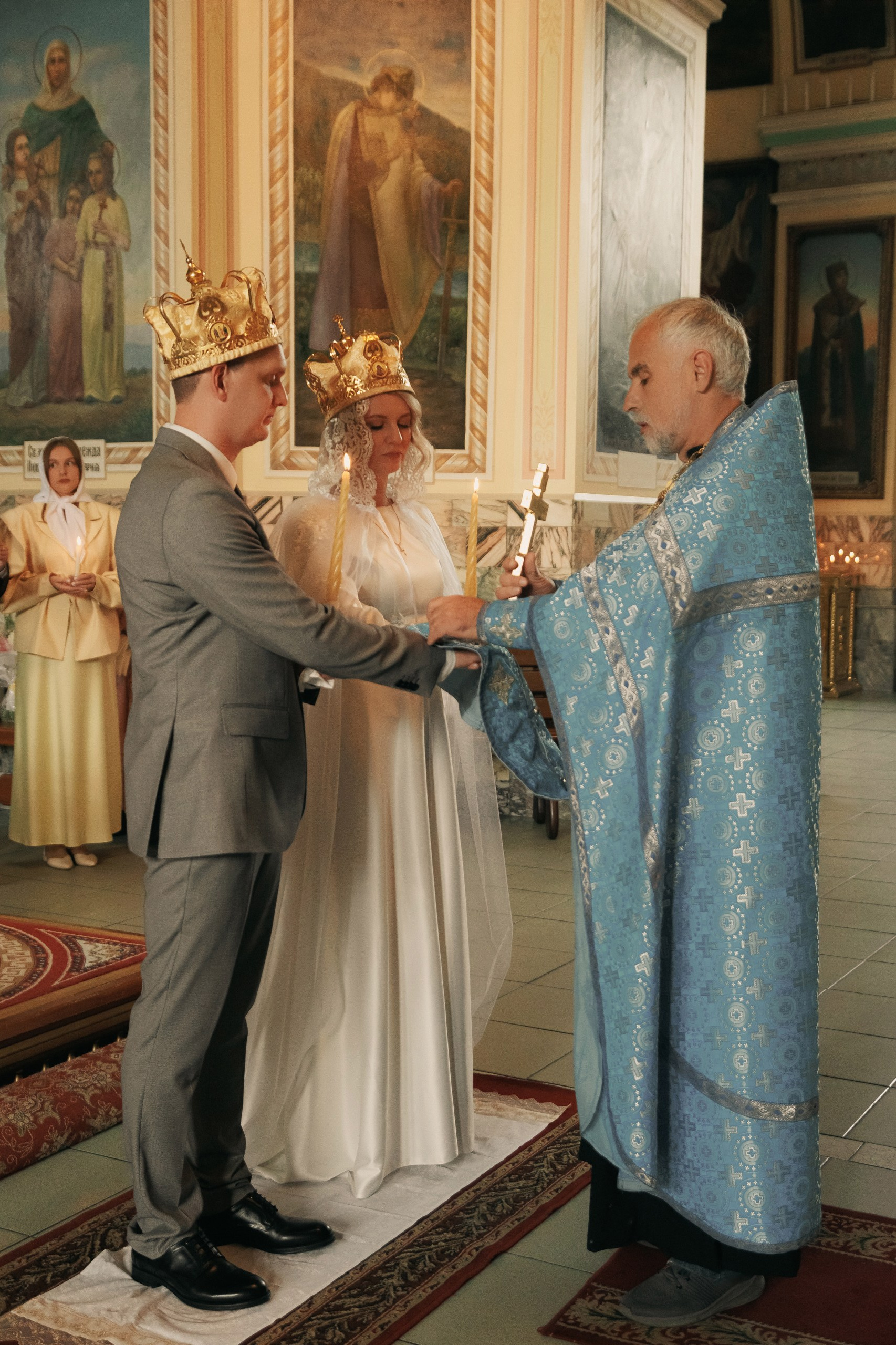Священник одевает венцы на головы молодожёнов у алтаря.