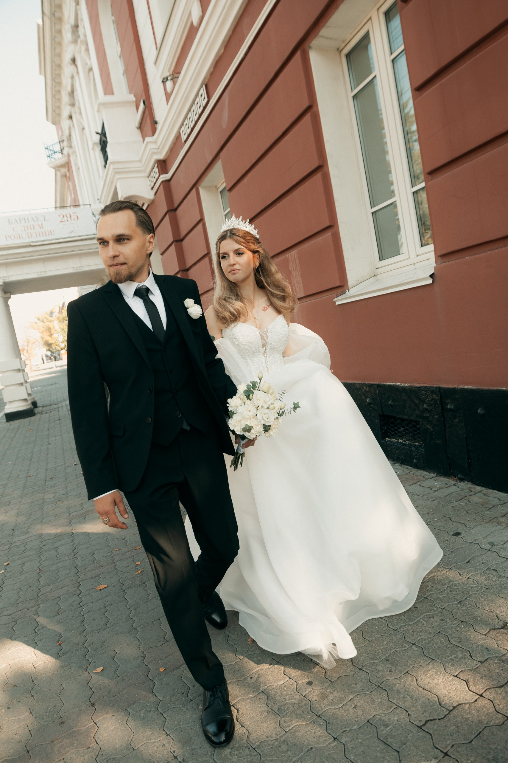 Пара идёт по улице, жених держит невесту за руку.