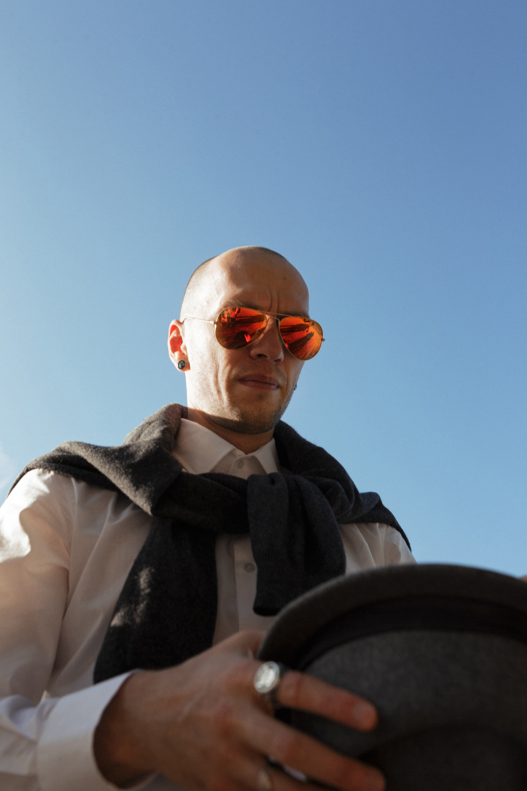 Жених  в белой рубашке и красных очках  смотрит на свою черную стильную шляпу.