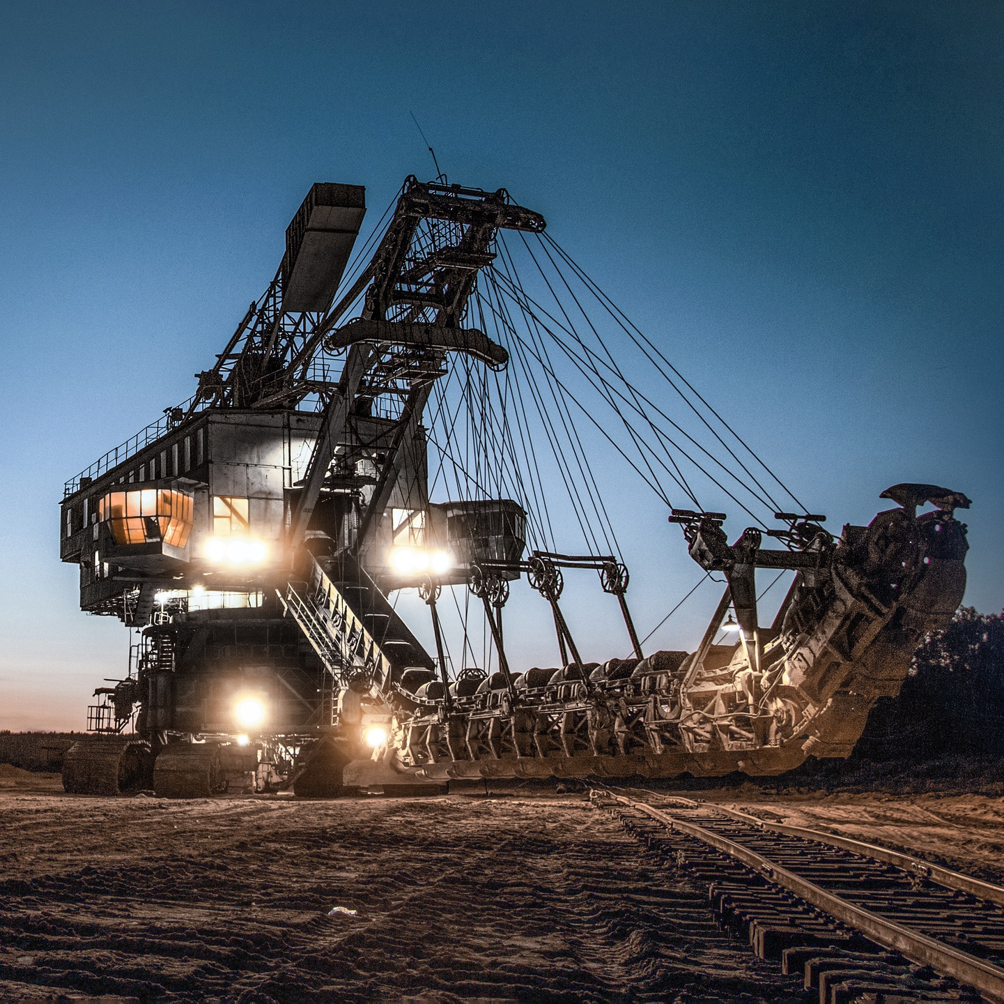 Карьерный экскаватор на открытом грунте с включёнными фарами, показывающий масштаб промышленной техники.