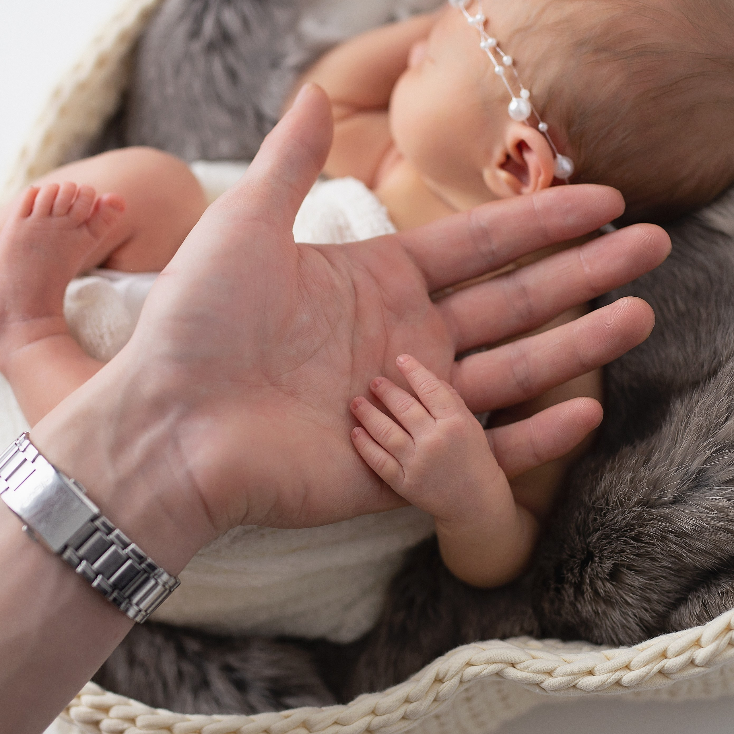 Большая ладонь папы держит ручки новорожденной малышки