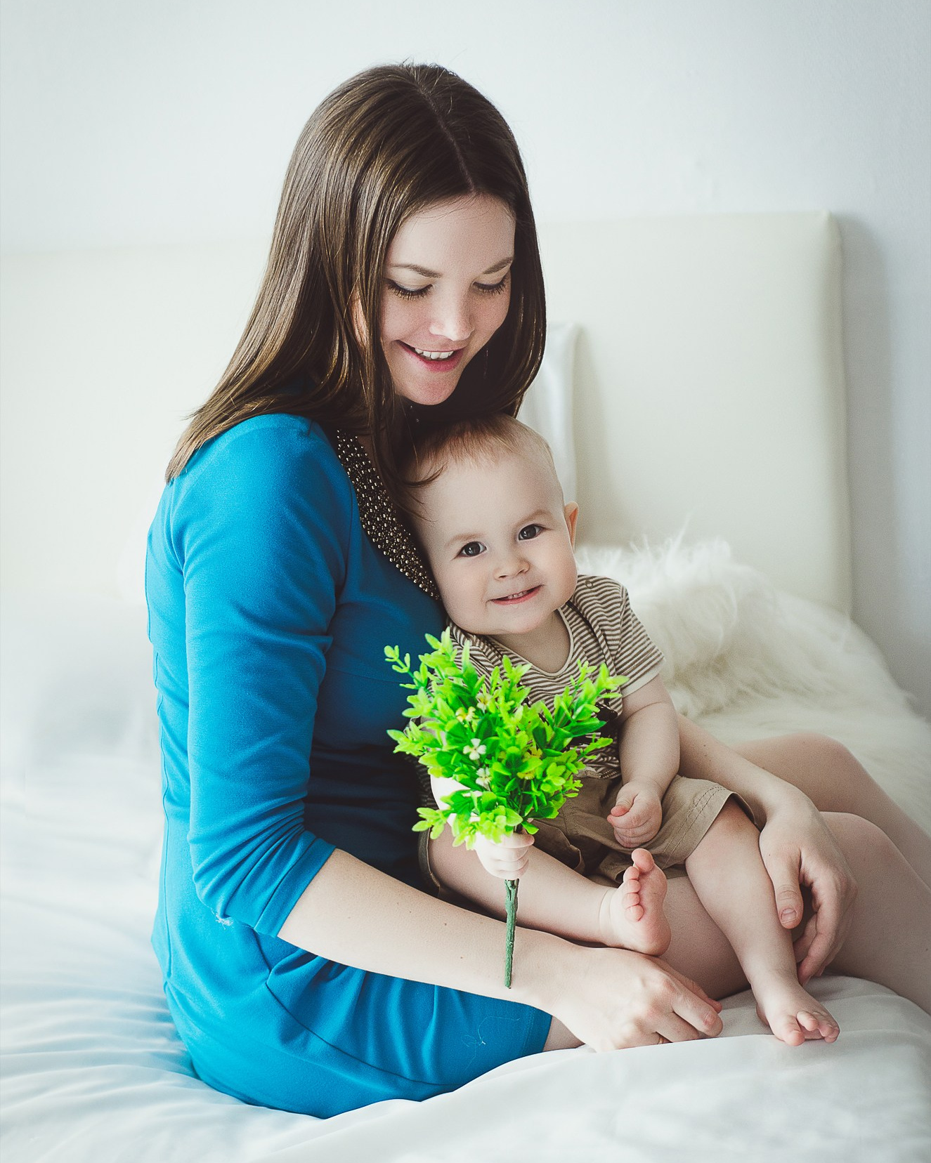 Детская фотосъемка - мама с малышом на кровати, держат зелёный букет, уютно.