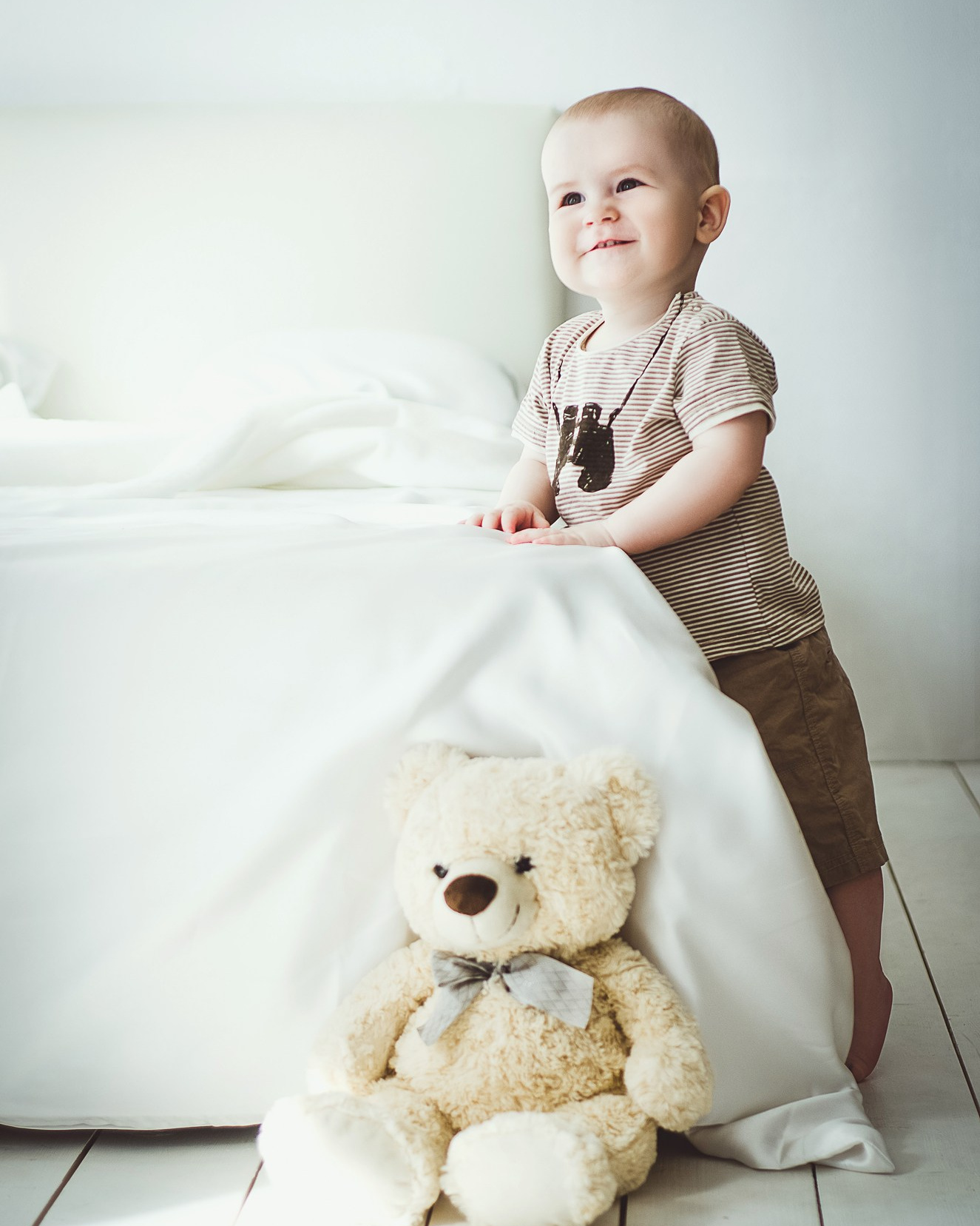 Детская фотосессия в студии - малыш у кровати в светлой уютной комнате с медвежонком.