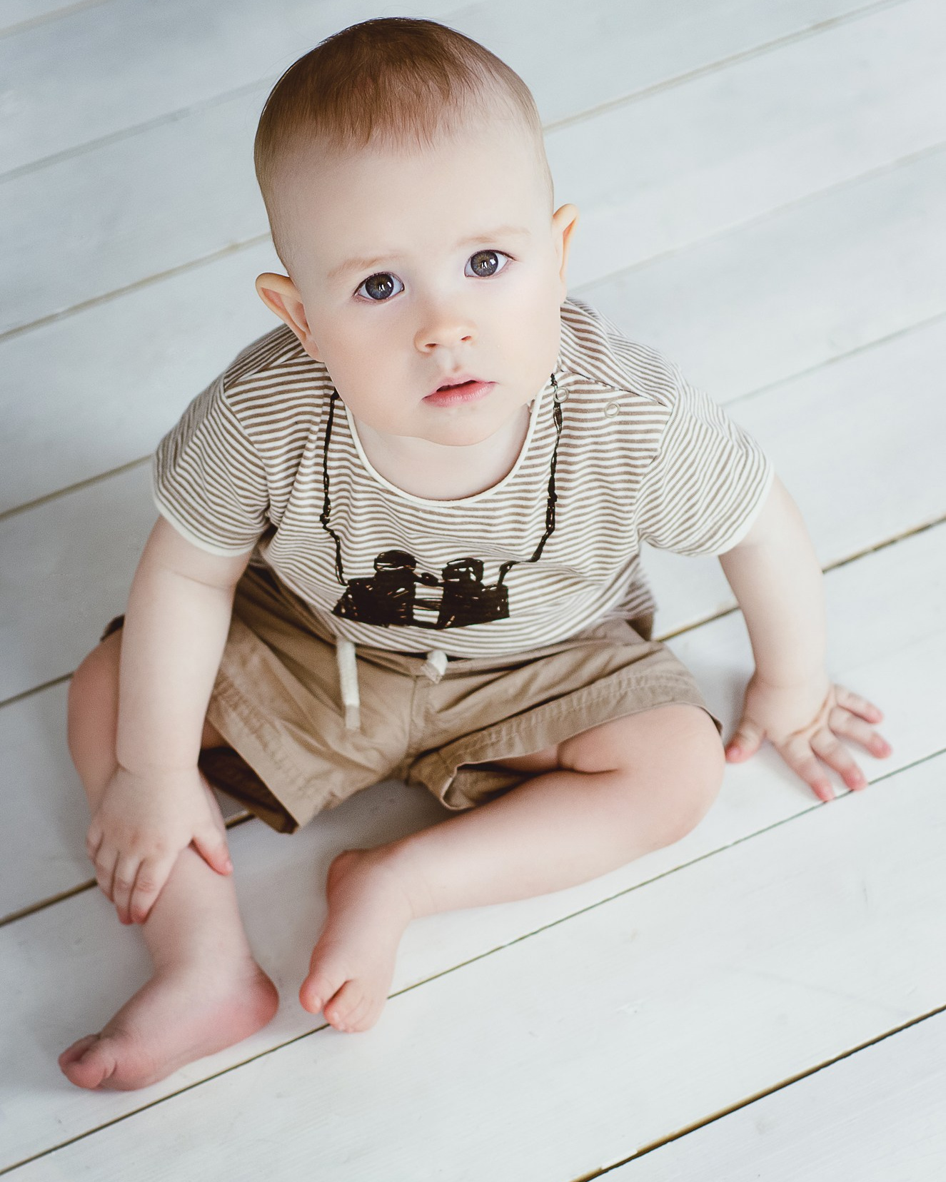 Фотограф Анна Шутова, фотосессия детей - малыш в полосатой футболке сидит на светлом деревянном полу.