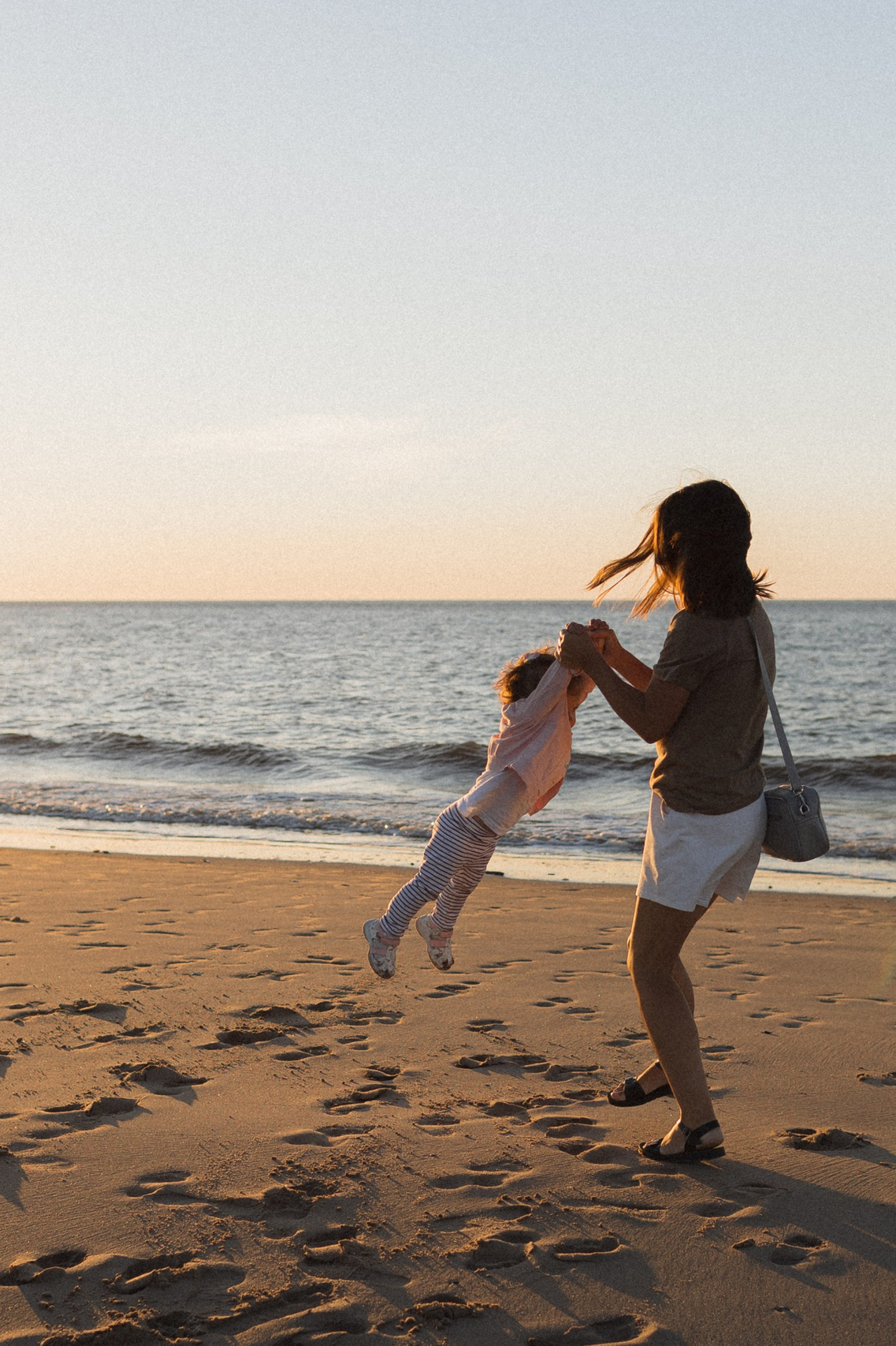 Семейные моменты в Архангельске, на Белом море: мать и дочь в нежных объятиях на песчаном пляже при закате с золотистыми бликами на воде