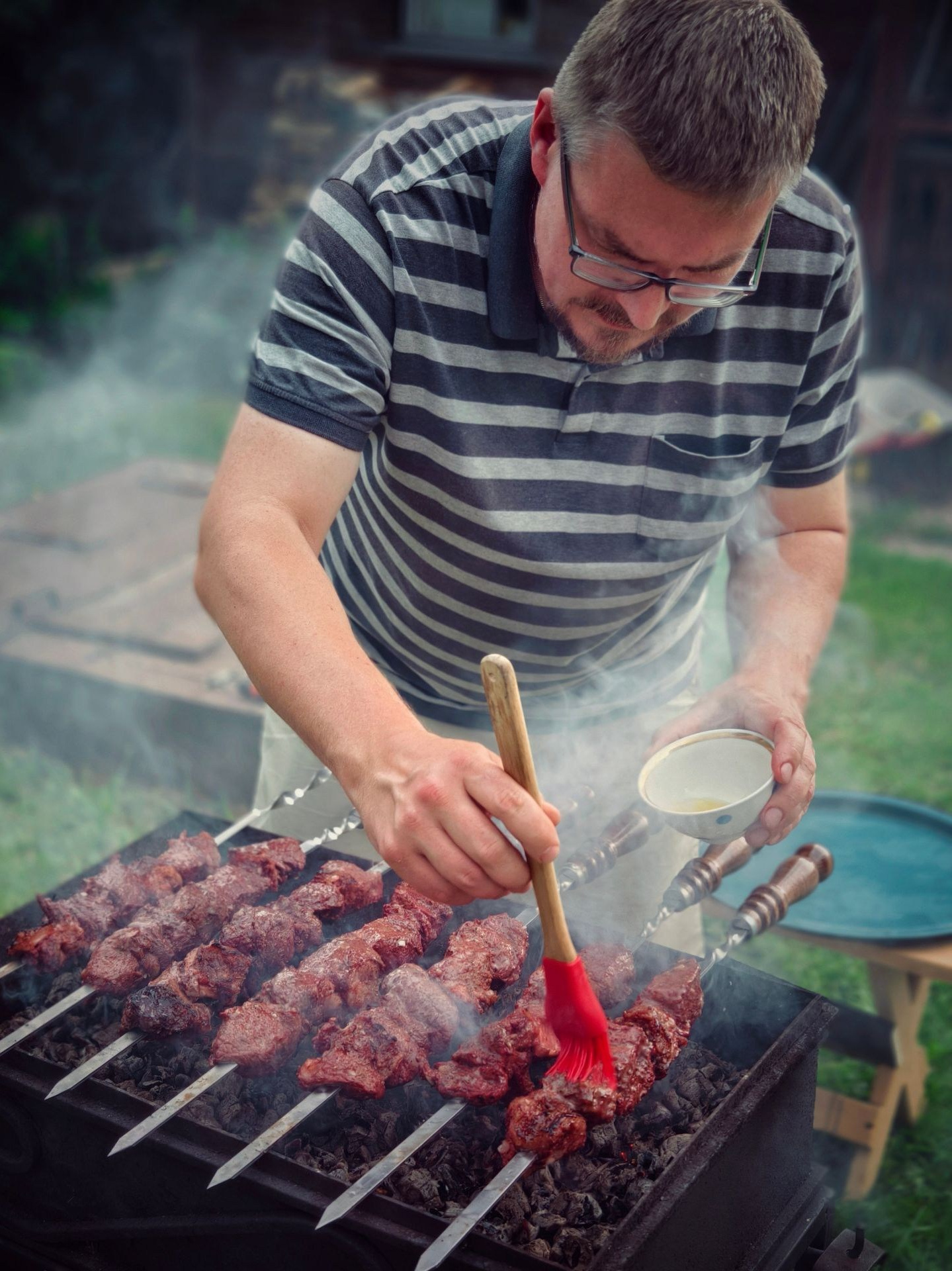 Мужчина готовит шашлыки на гриле в саду