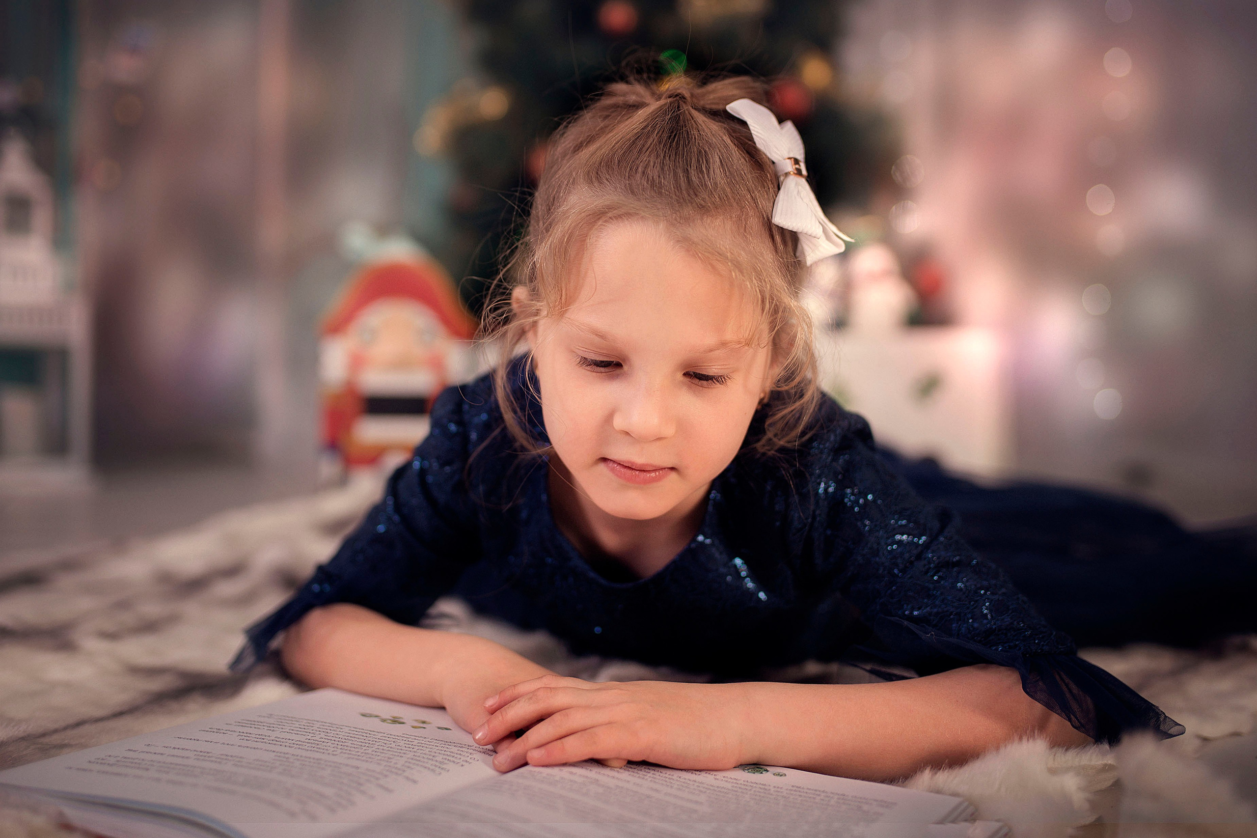 Девочка лежит у новогодней ёлки и читает книгу