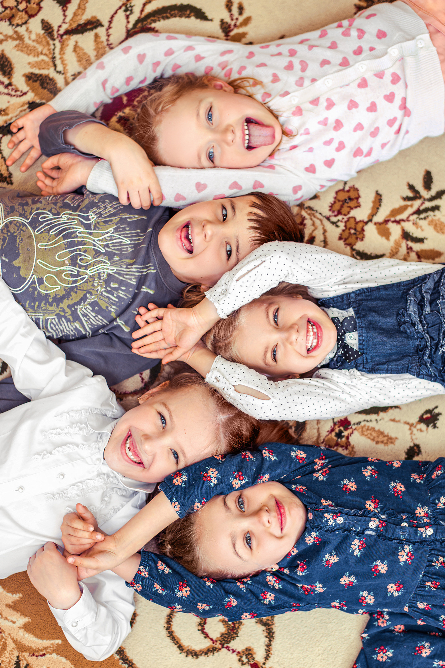 Улыбающиеся дети лежат на полу, держась за руки.