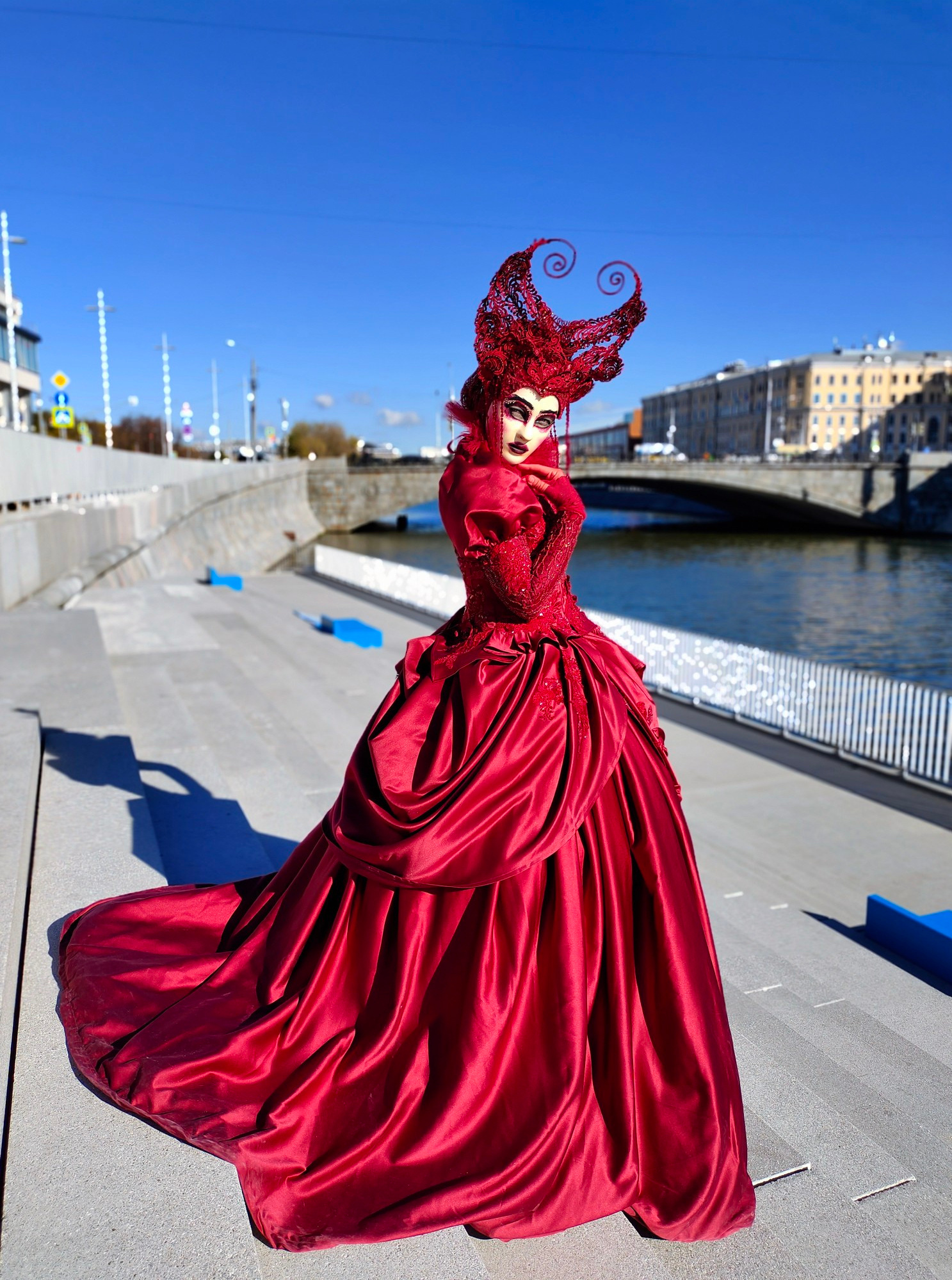Мим в бордовом платье встречает гостей на набережной реки Москва.