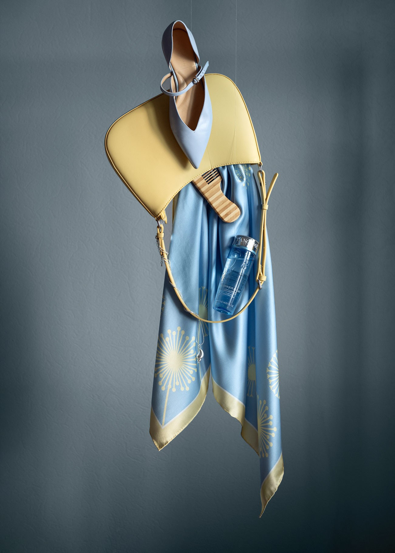 Креативное предметное фото: сумка висит в воздухе. а из нее вываливаются предметы: шелковый платок, расческа, лосьон и украшение