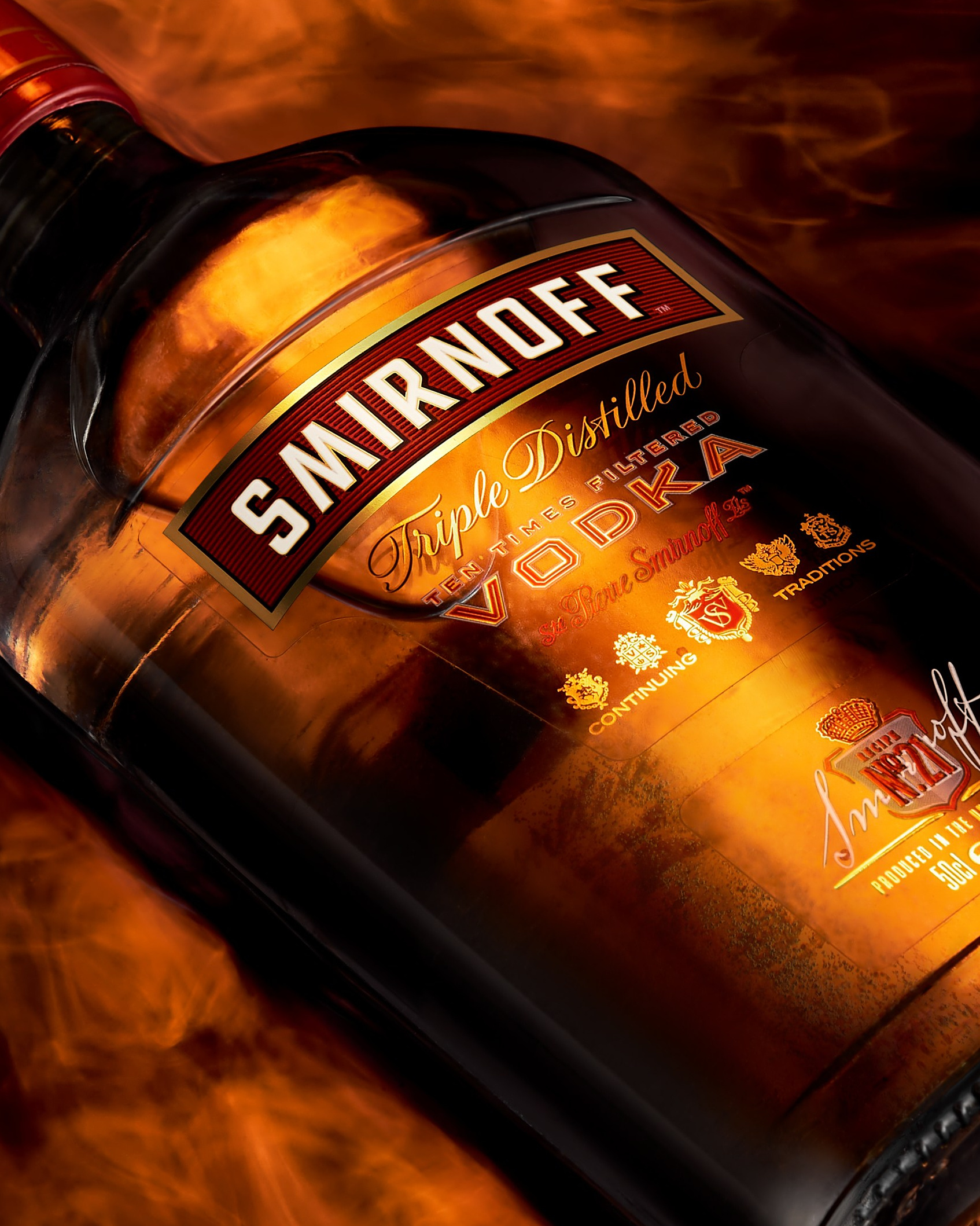 Яркая предметная фотография бутылки Smirnoff с огненными бликами на фоне, пример классического «глянцевого» стиля в рекламе. Иллюстрация к разделу о визуальной перенасыщенности и смене эстетики в современной предметной фотографии.