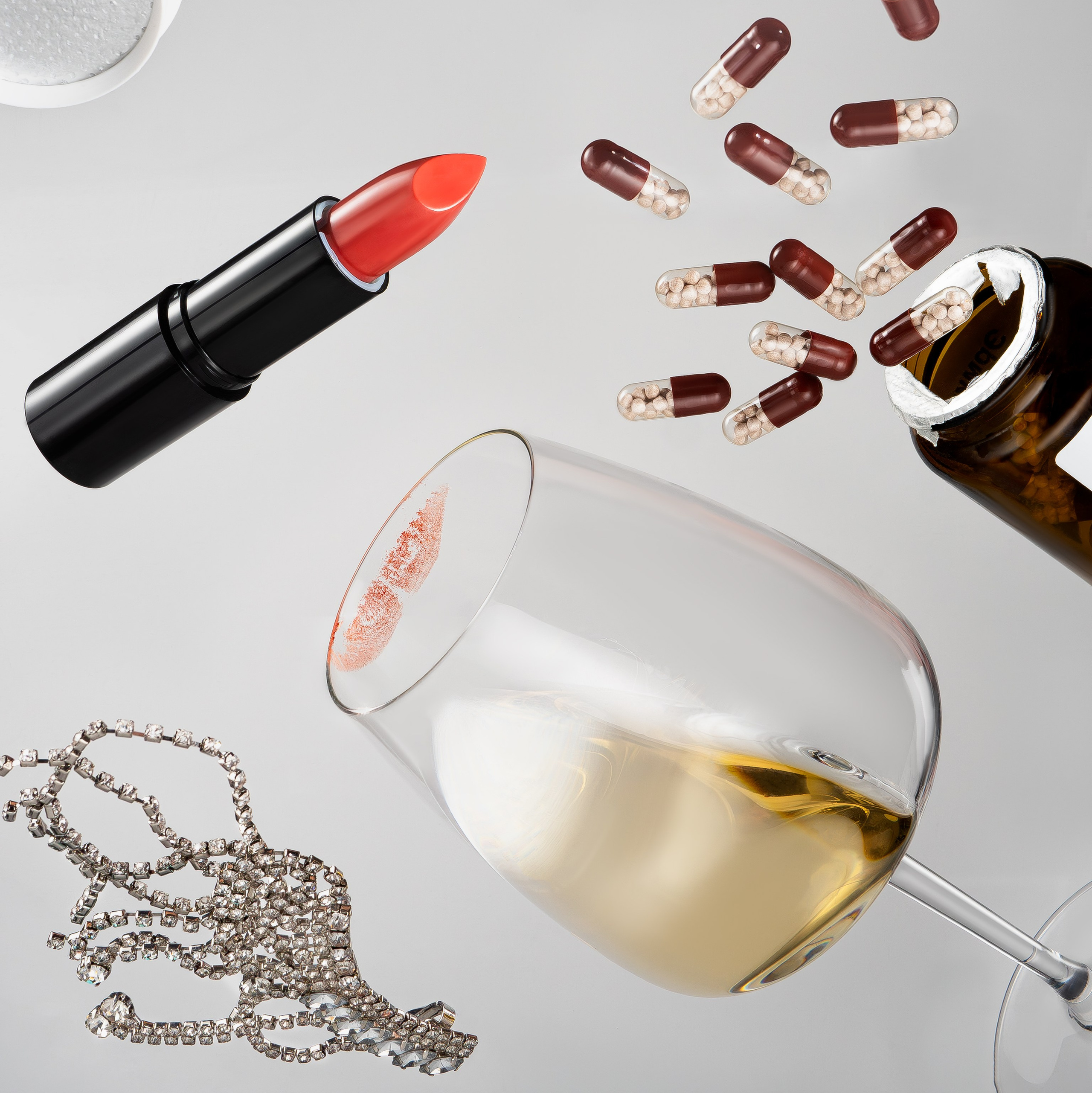 Фото из под стеклянного стола, на котором лежит опрокинутый бокал вина, разбросаны таблетки, губная помада и аксессуры