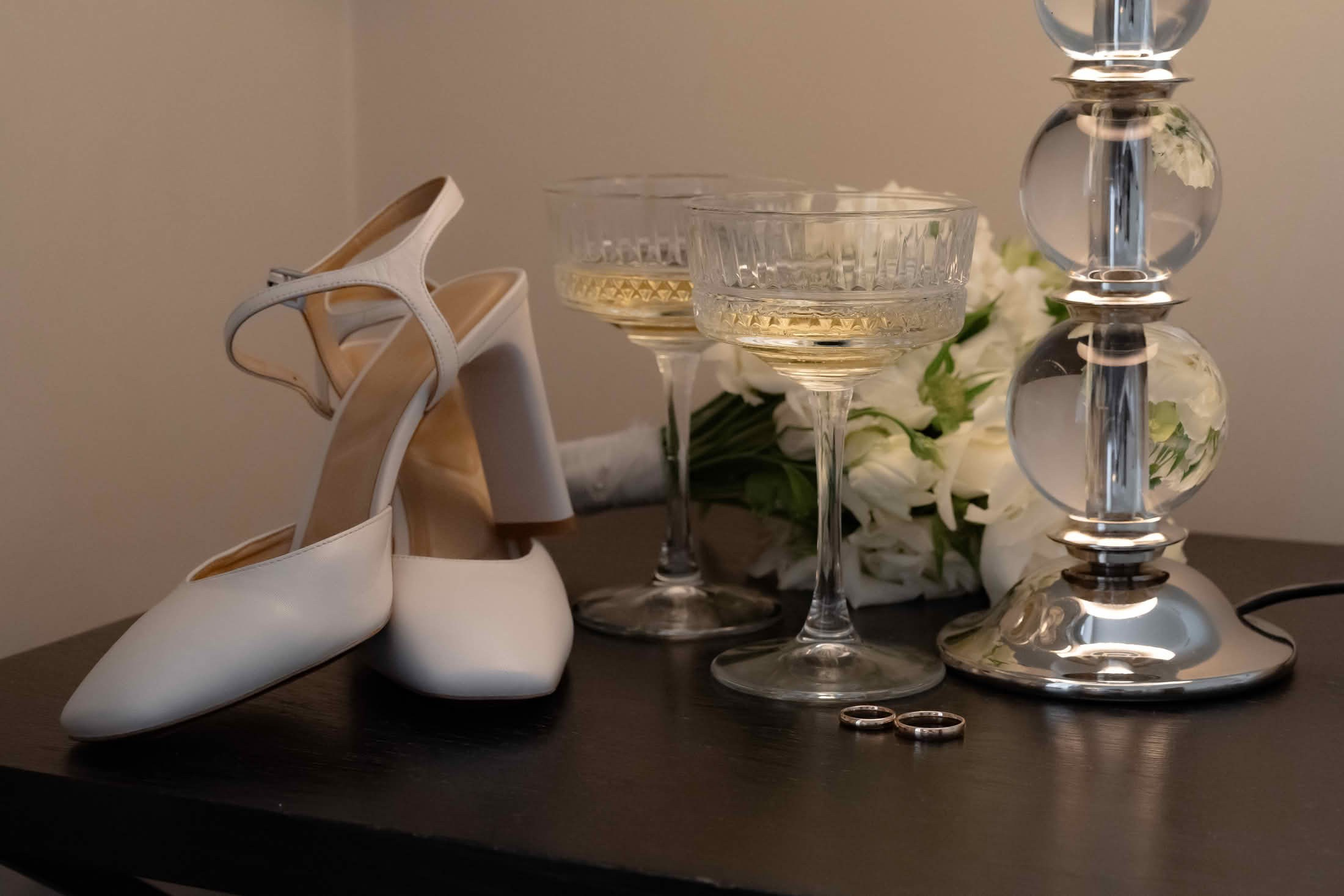Белые свадебные туфли и букет невесты на тёмном столике в отеле.