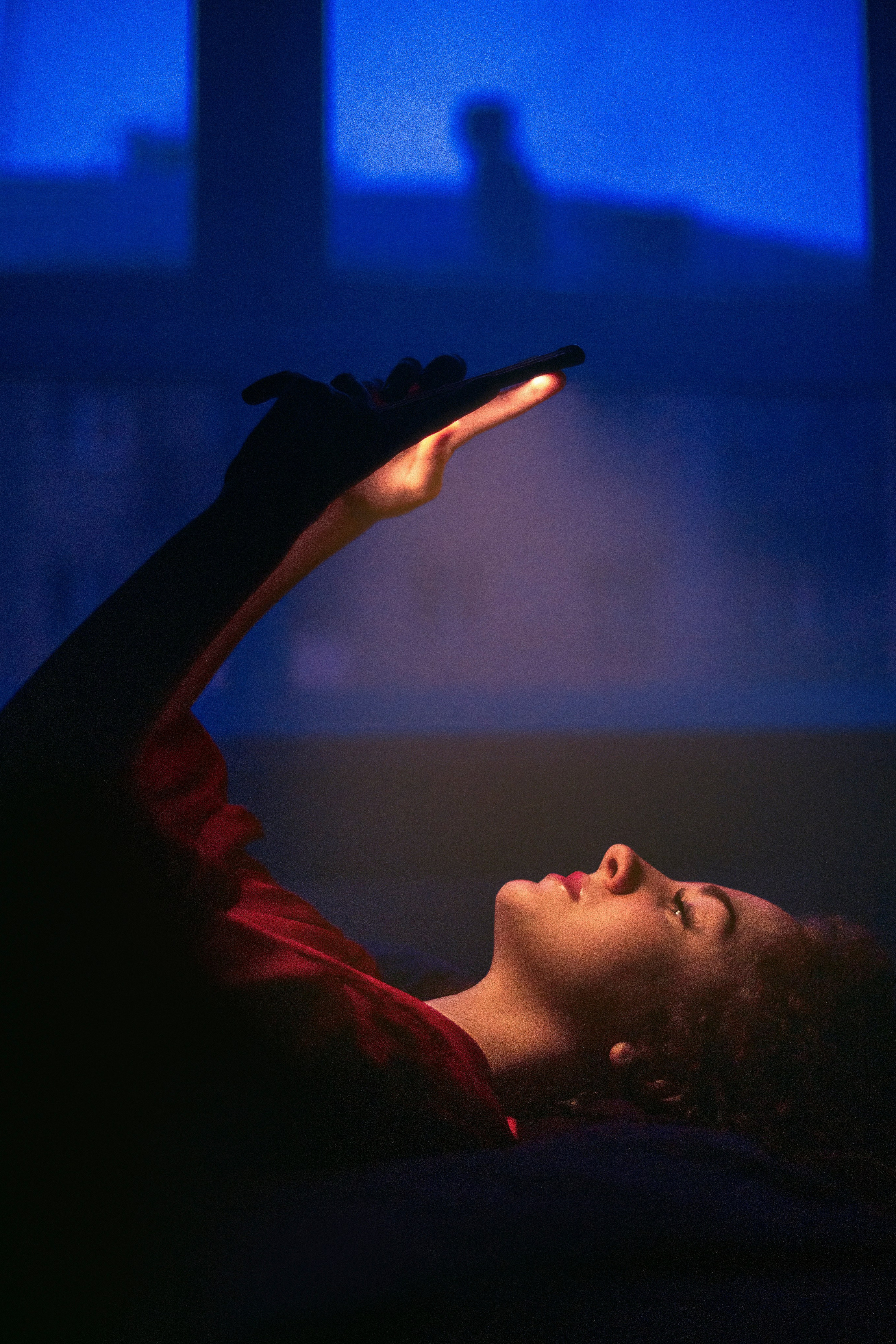 A woman lying in bed illuminated by a smartphone screen, creating an atmospheric night shot, perfect for visual content and social marketing strategy.